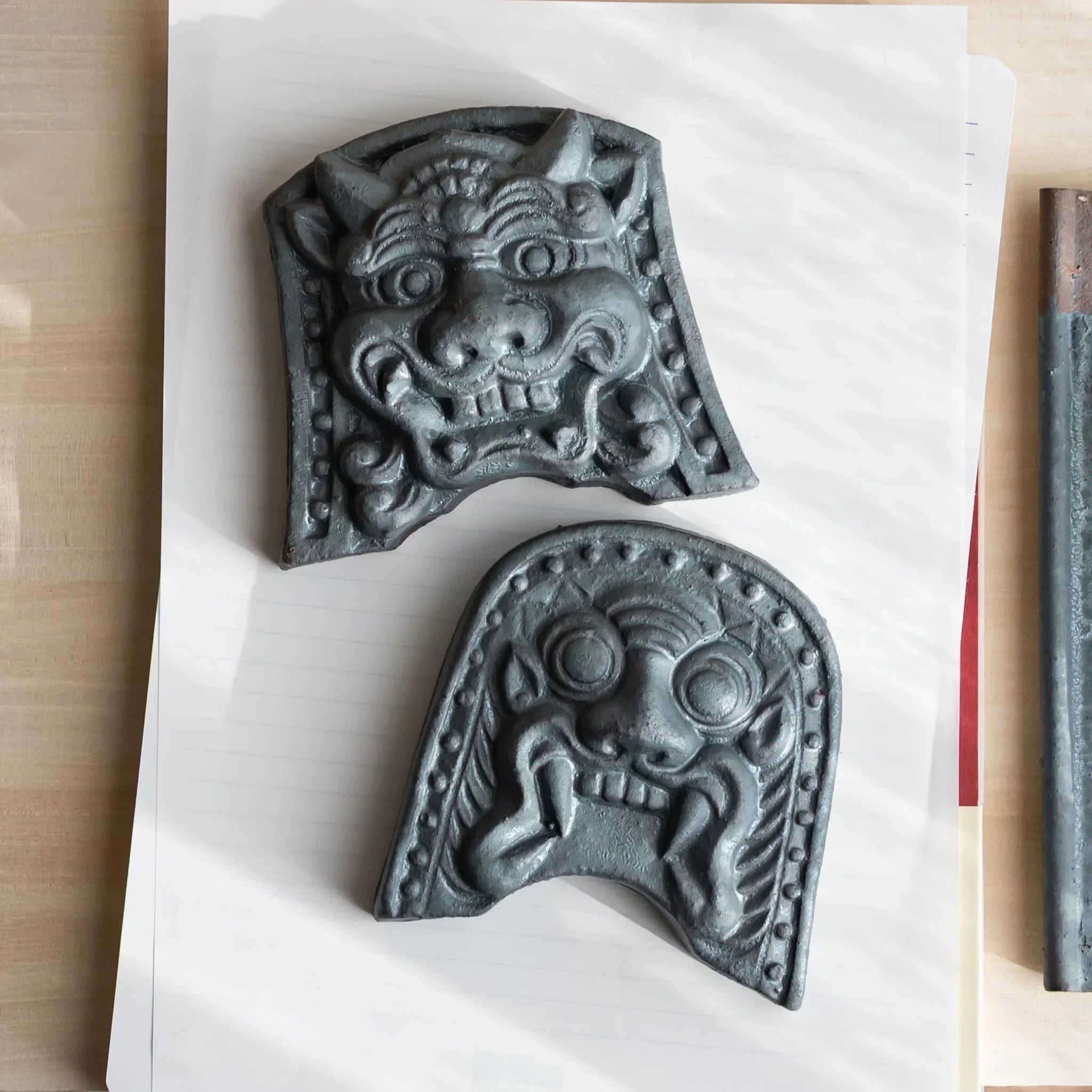 Japanese Paperweight Desk Accessory set with two oni roof guardian ceramic tiles on lined paper with pen rod.