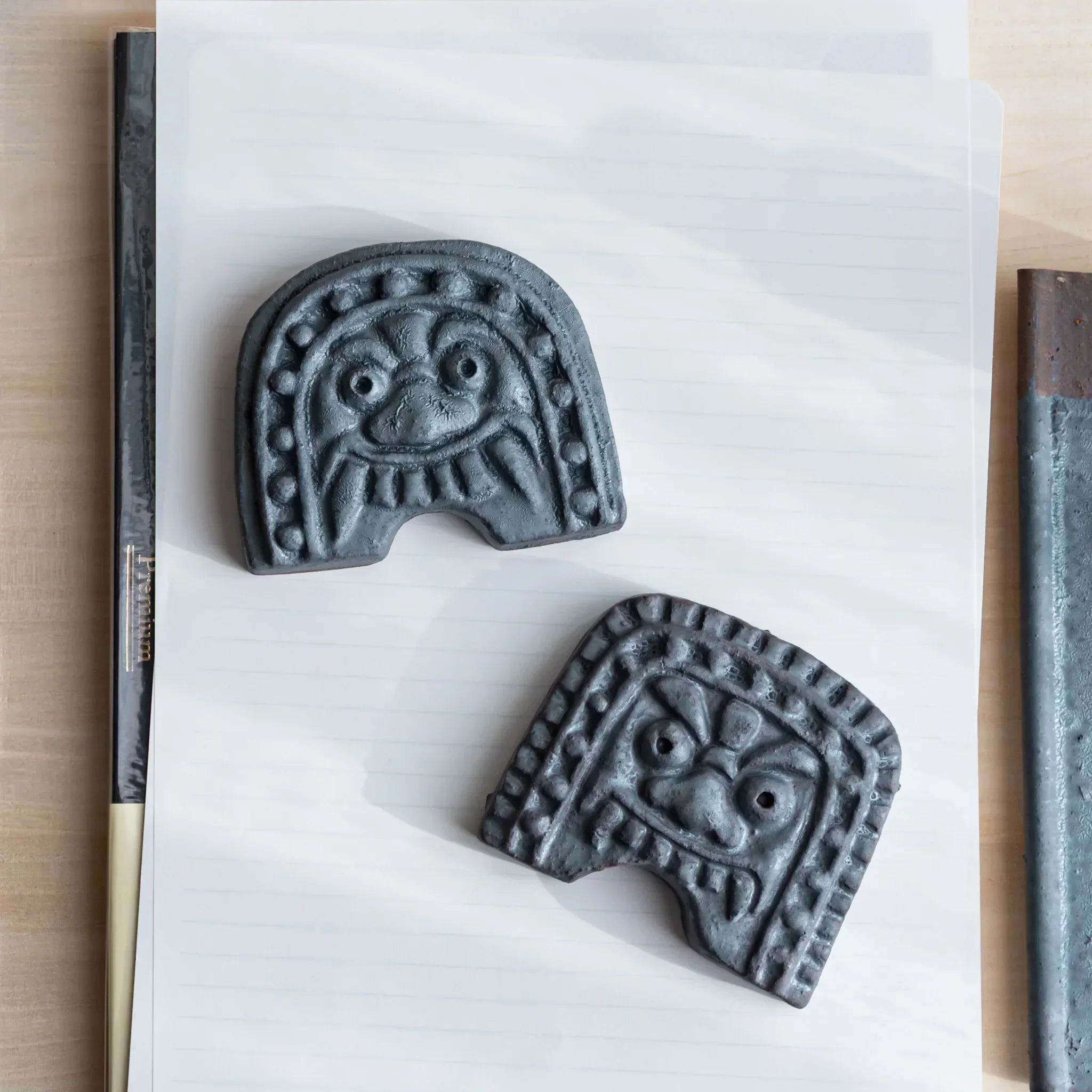Two Japanese Paperweights inspired by Oni-gawara roof tiles placed on paper, ceramic pieces as refined Desk Accessories.