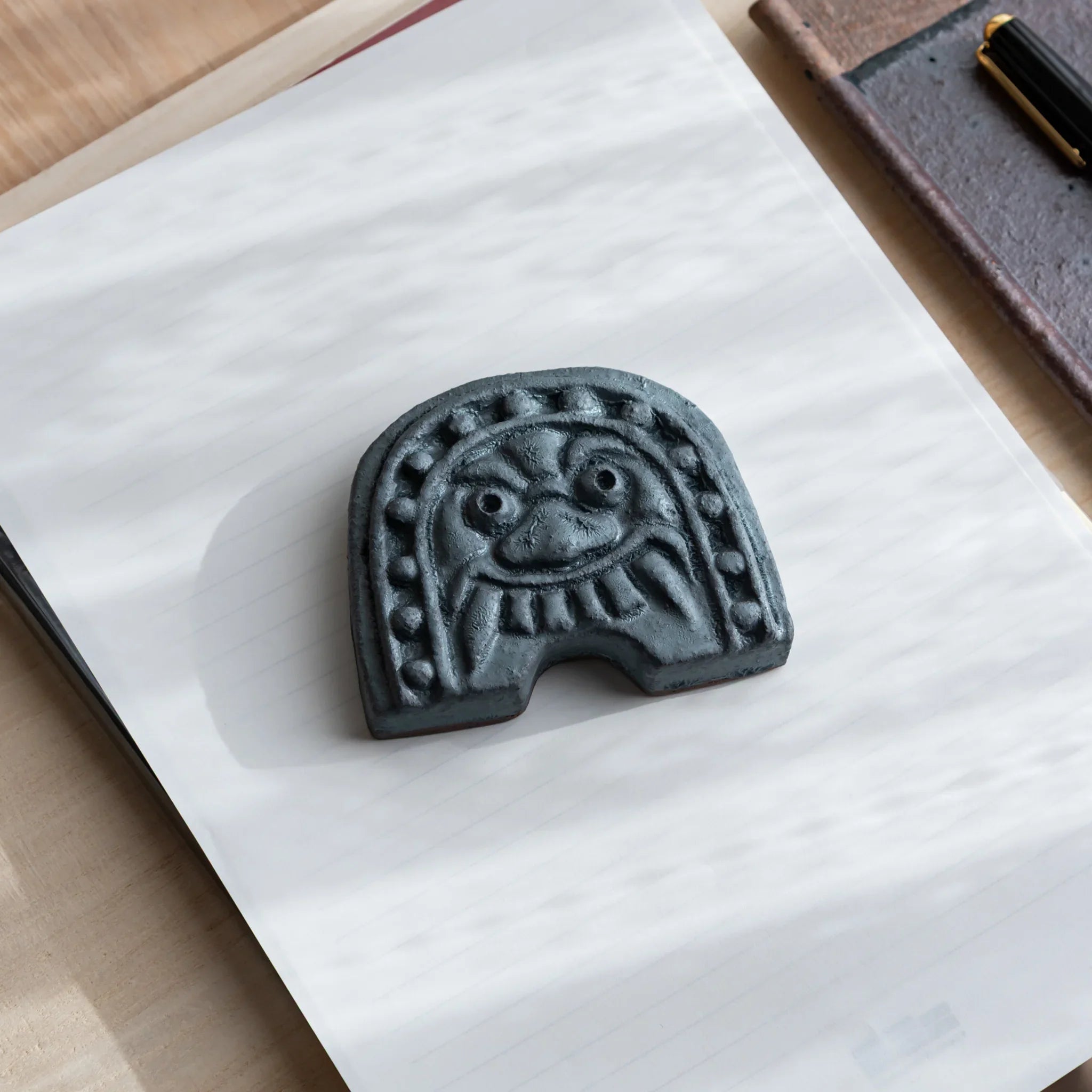 Japanese Paperweight inspired by Oni-gawara roof tiles resting on paper beside a fountain pen as a refined Desk Accessory.