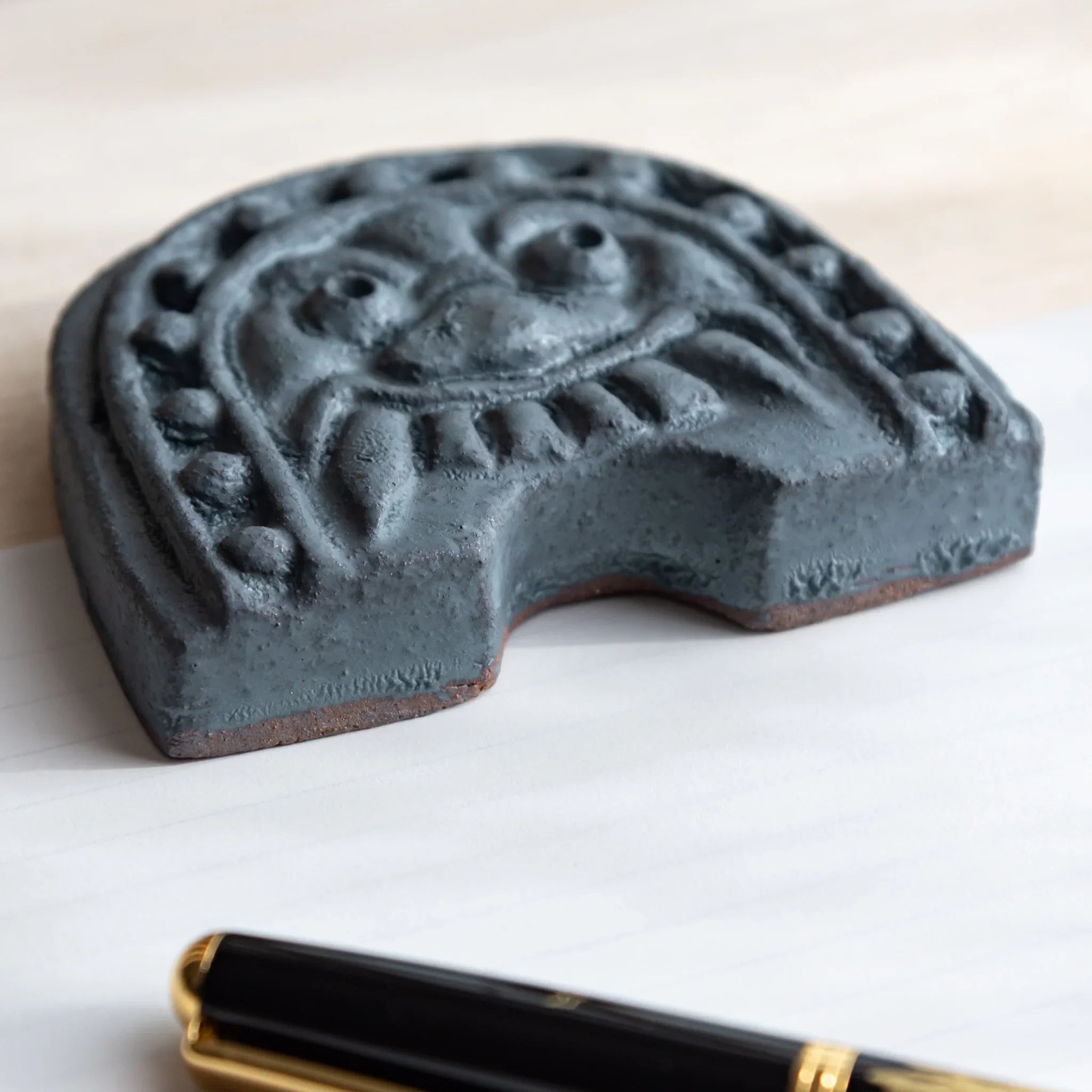 Handcrafted Japanese paperweight inspired by Oni-gawara roof tiles, beside a Japanese Fountain Pen on white paper.