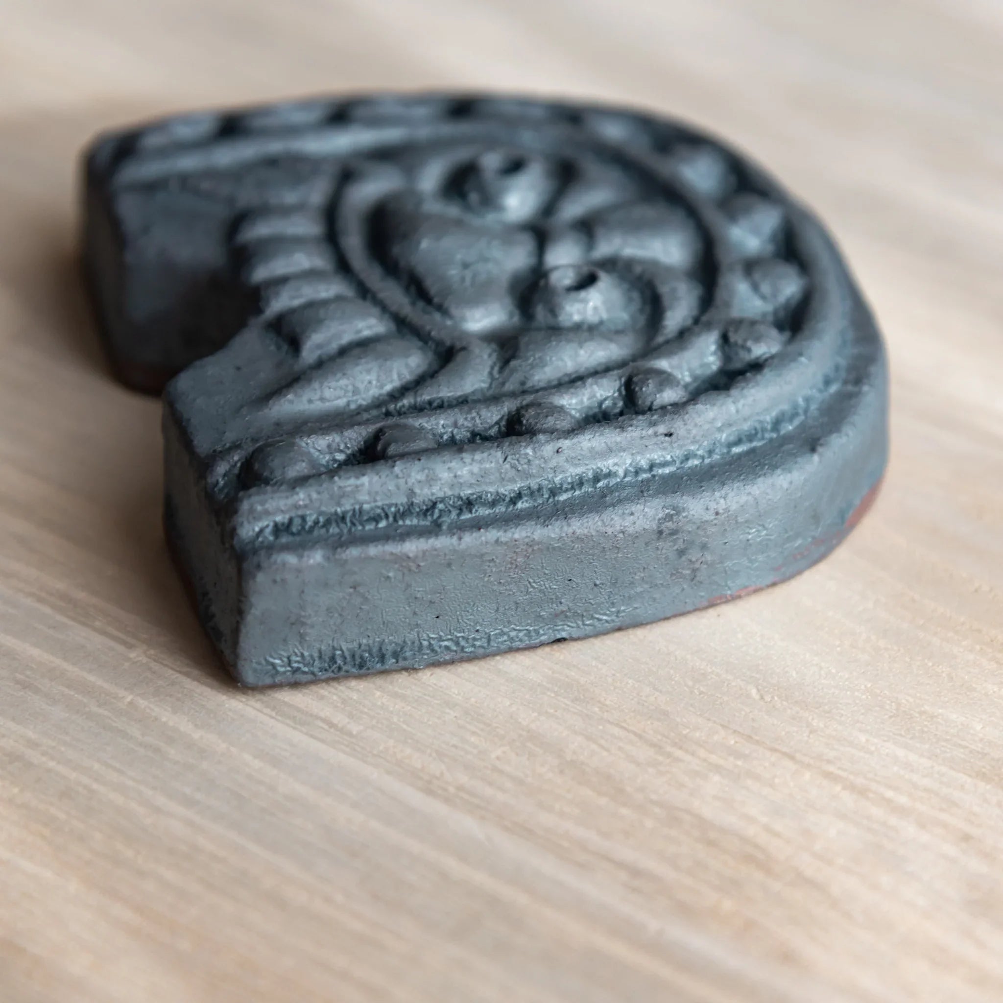 Handcrafted Japanese Kawara Roof Guardian Paperweight with a rounded face design on a wooden desk, made from gray ceramic.