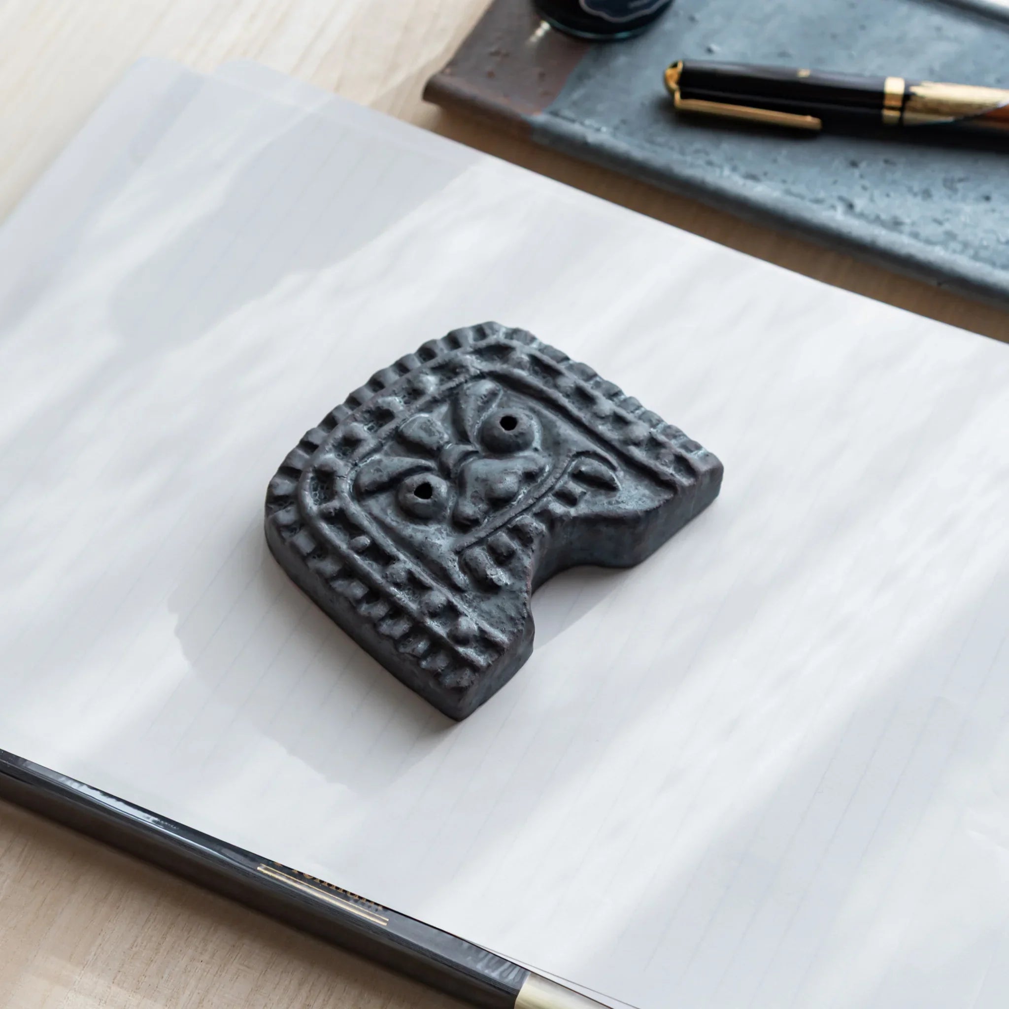Japanese Paperweight inspired by Oni-gawara roof tiles resting on paper beside a fountain pen as a refined Desk Accessory.