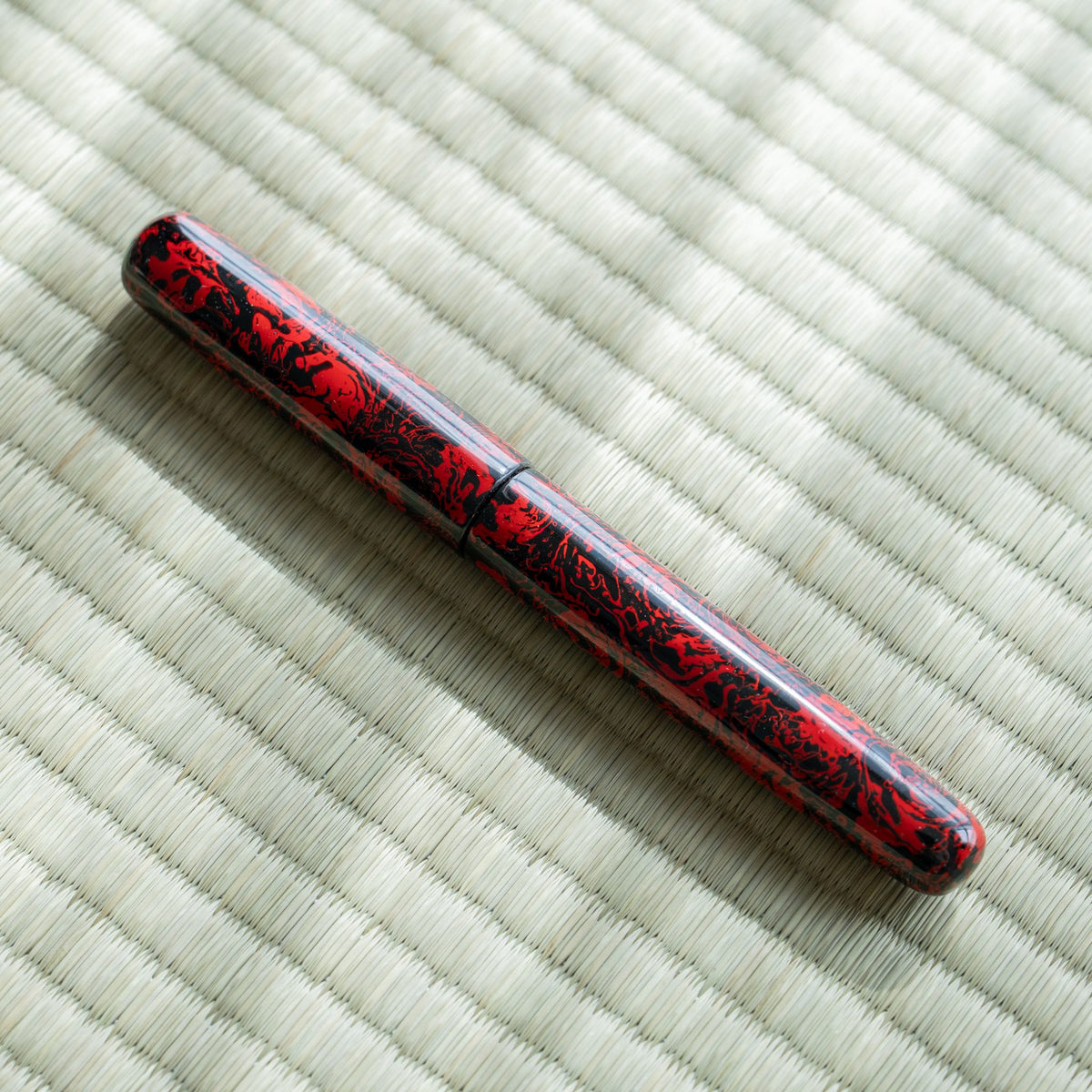 Capped Kagaribi Tsugaru-nuri fountain pen lying diagonally on tatami in sunlight, red and black urushi pattern