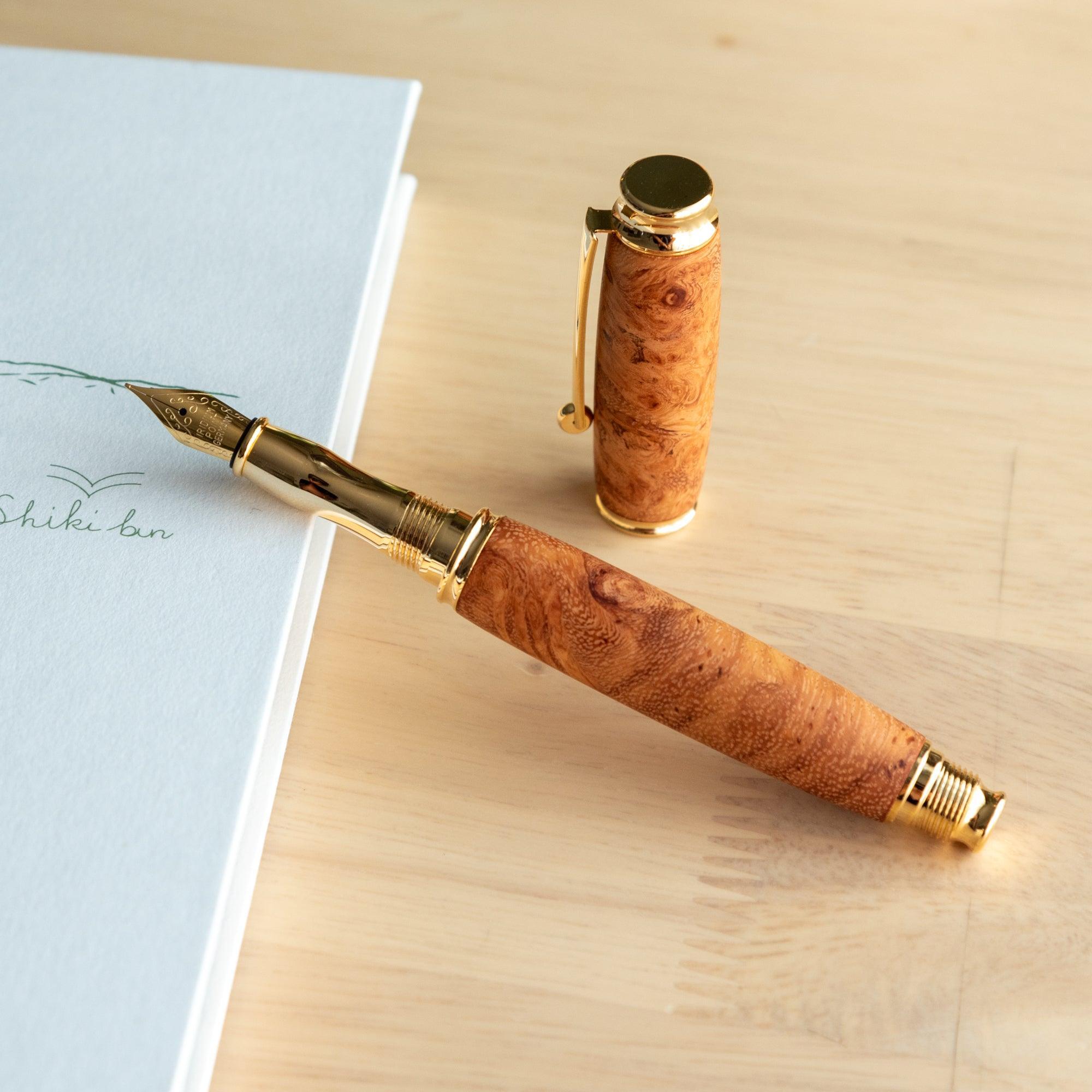 A Japanese fountain pen made of Karin wood with gold details, its cap removed, placed on a notebook to highlight the nib and intricate craftsmanship.