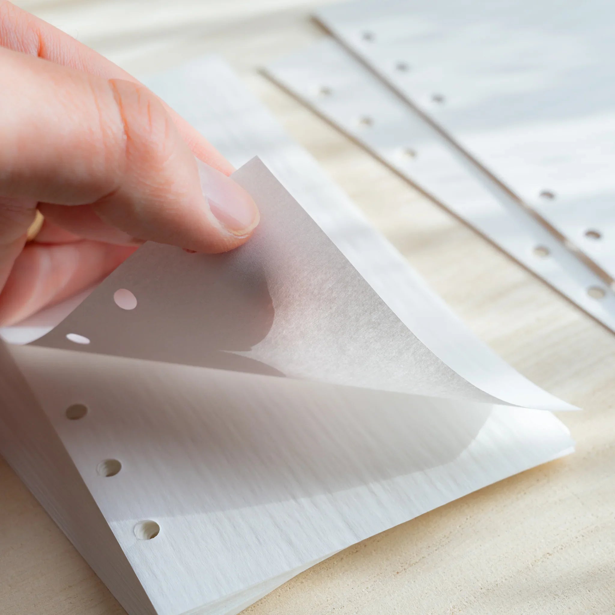 Hand lifting a thin Japanese Stationery white onion skin planner sheet, showing its translucent texture and six-hole punches.
