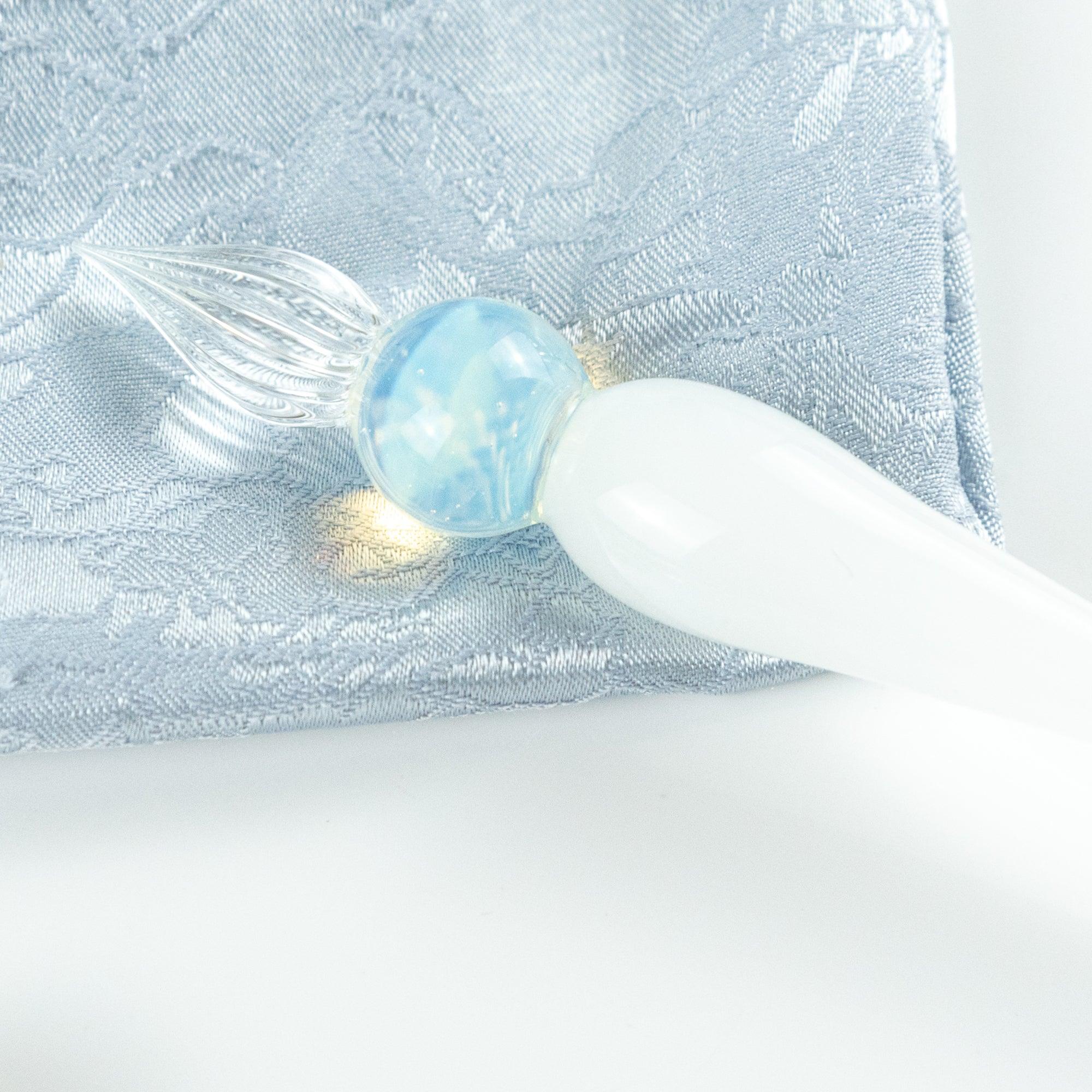 Close-up of a glass pen with white handle and blue sphere, placed on silver fabric. Ideal for lovers of Japanese stationery.