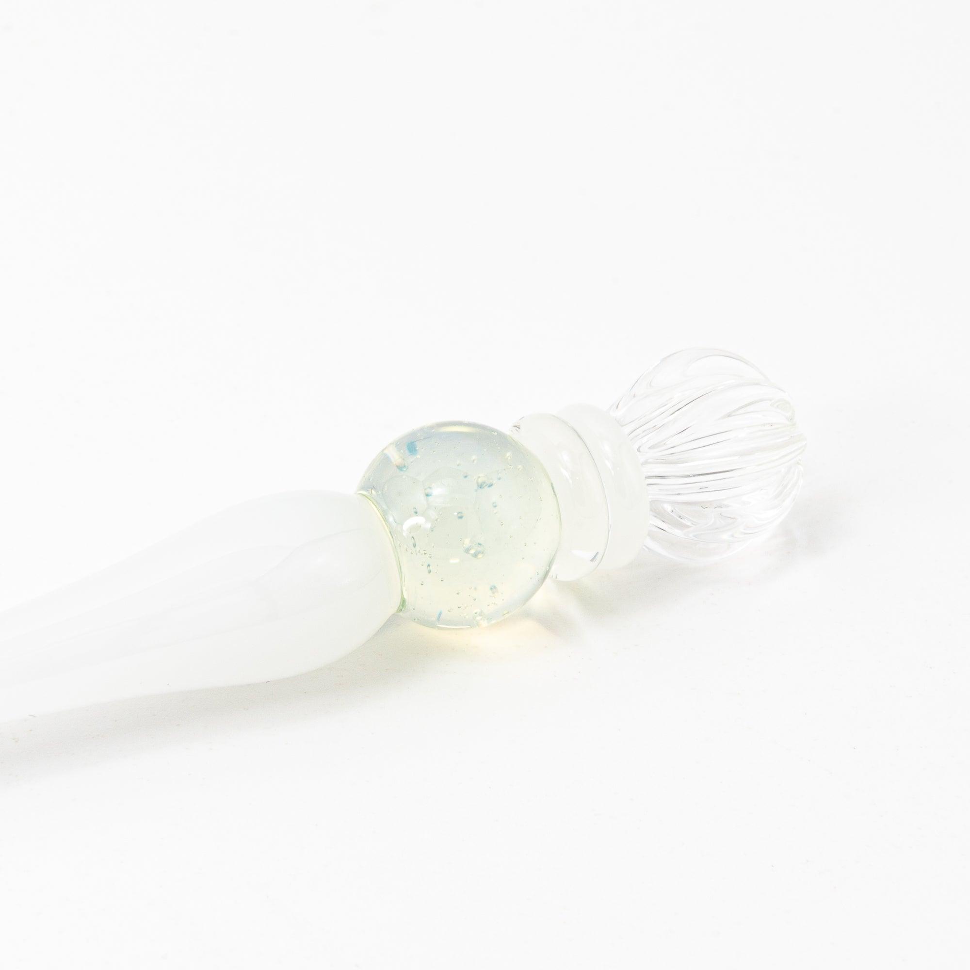 White glass pen with clear and blue spheres, elegantly poised on a pristine surface, perfect for stationery lovers.