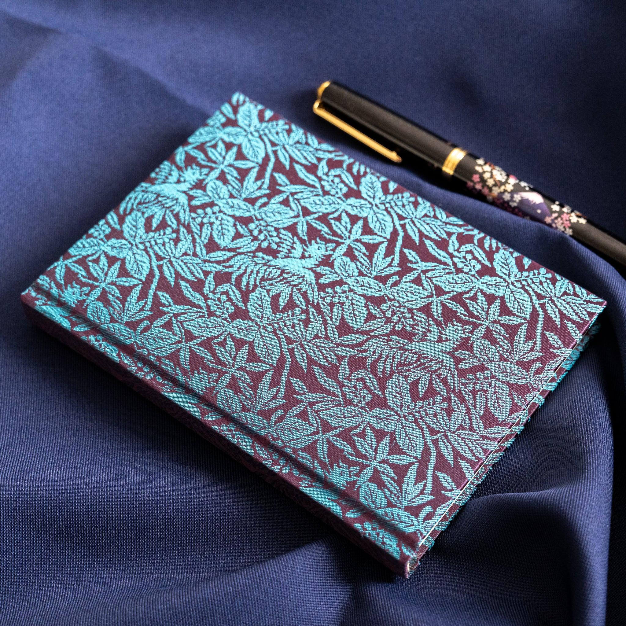 Kiri Take Ho-o Nishijin silk notebook close-up overhead view with maki-e pen resting on teal leaf patterned cover