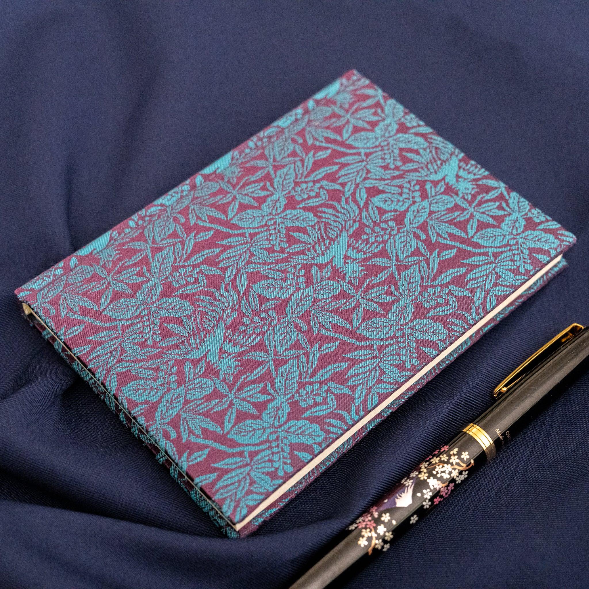 Kiri Take Ho-o Nishijin silk notebook overhead view with maki-e fountain pen below on navy fabric, lifestyle shot