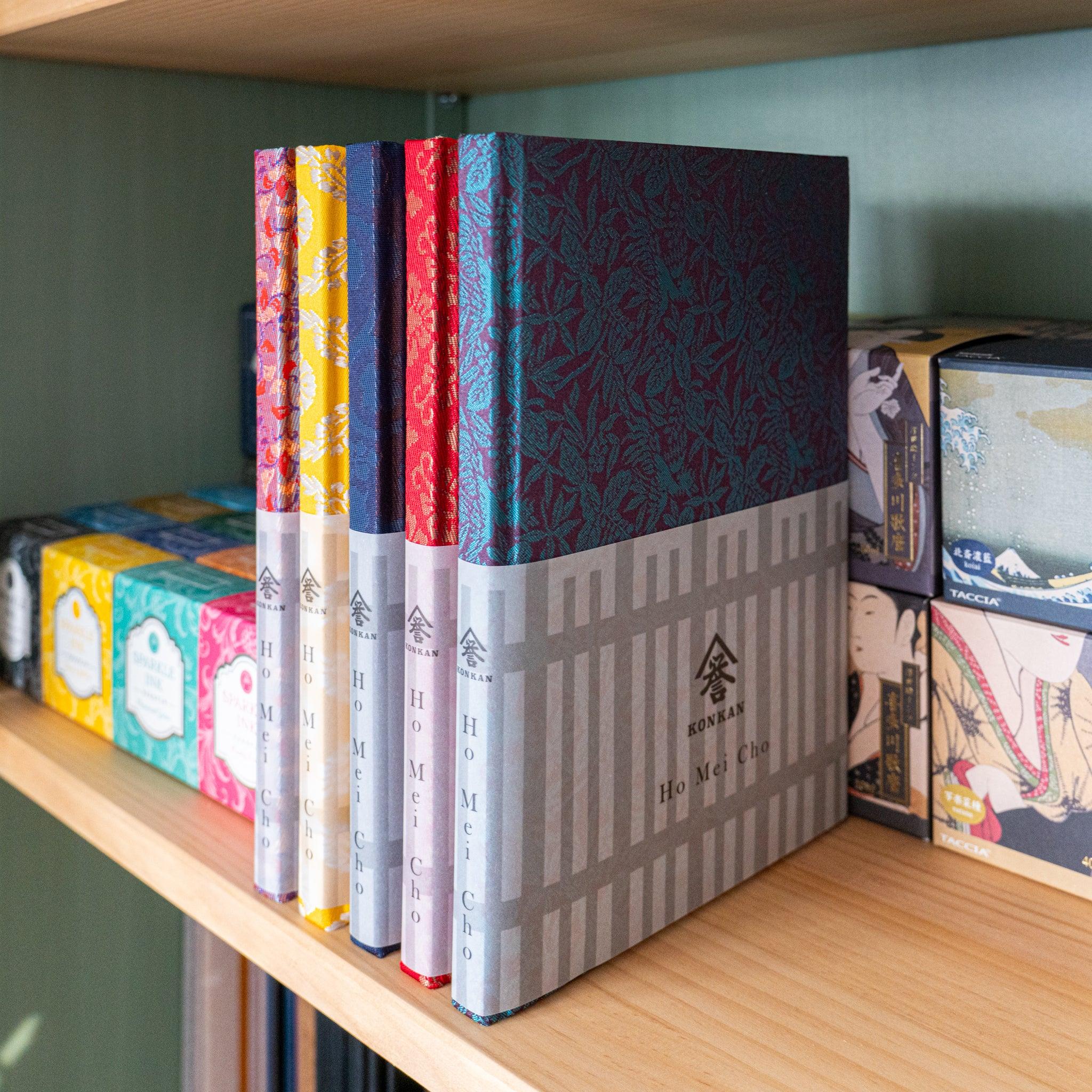 Kiri Take Ho-o Nishijin silk Homeicho notebooks in multiple colorways standing on wooden shelf with Konkan paper bands