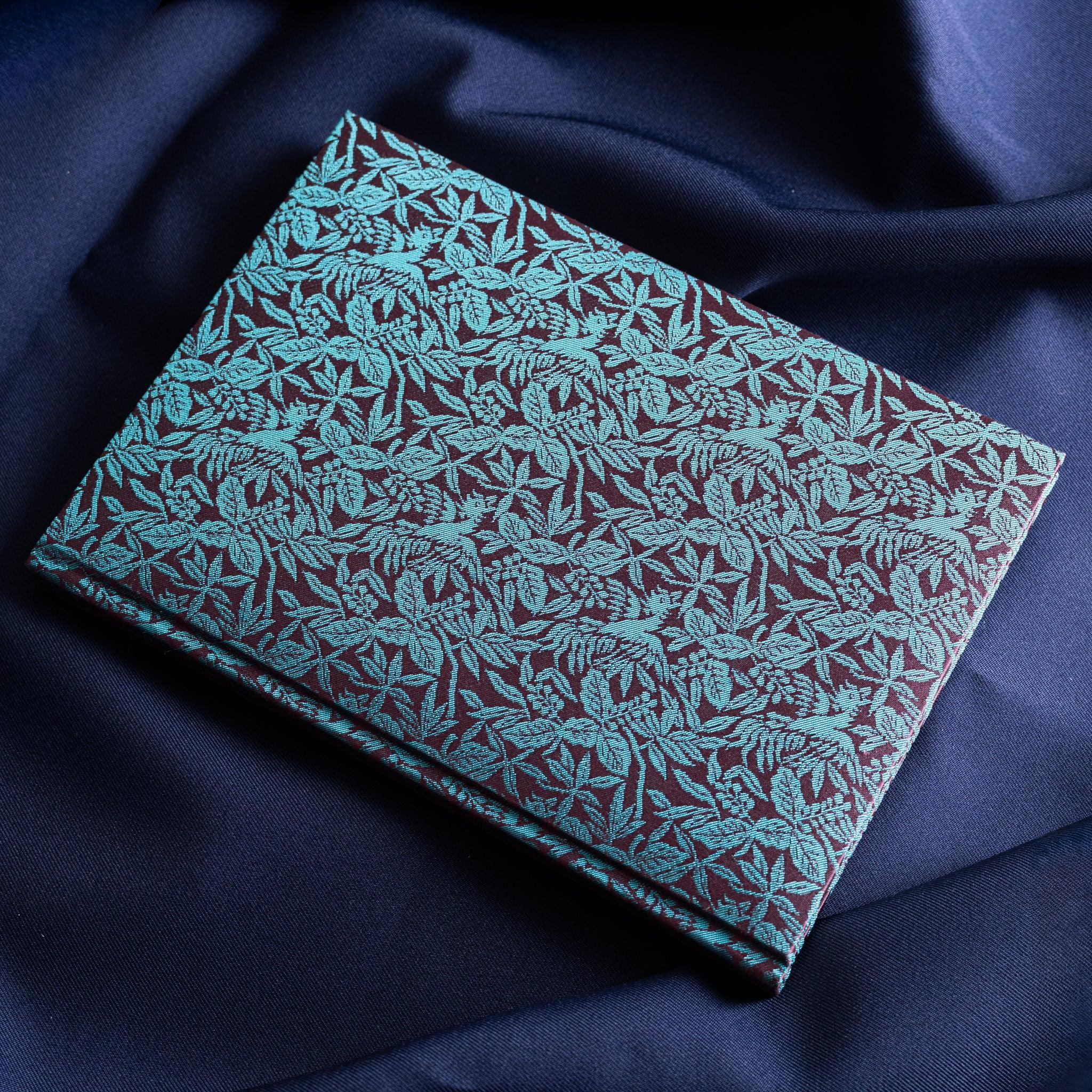 Kiri Take Ho-o Nishijin silk Homeicho notebook angled view showing teal and maroon woven silk cover on navy fabric