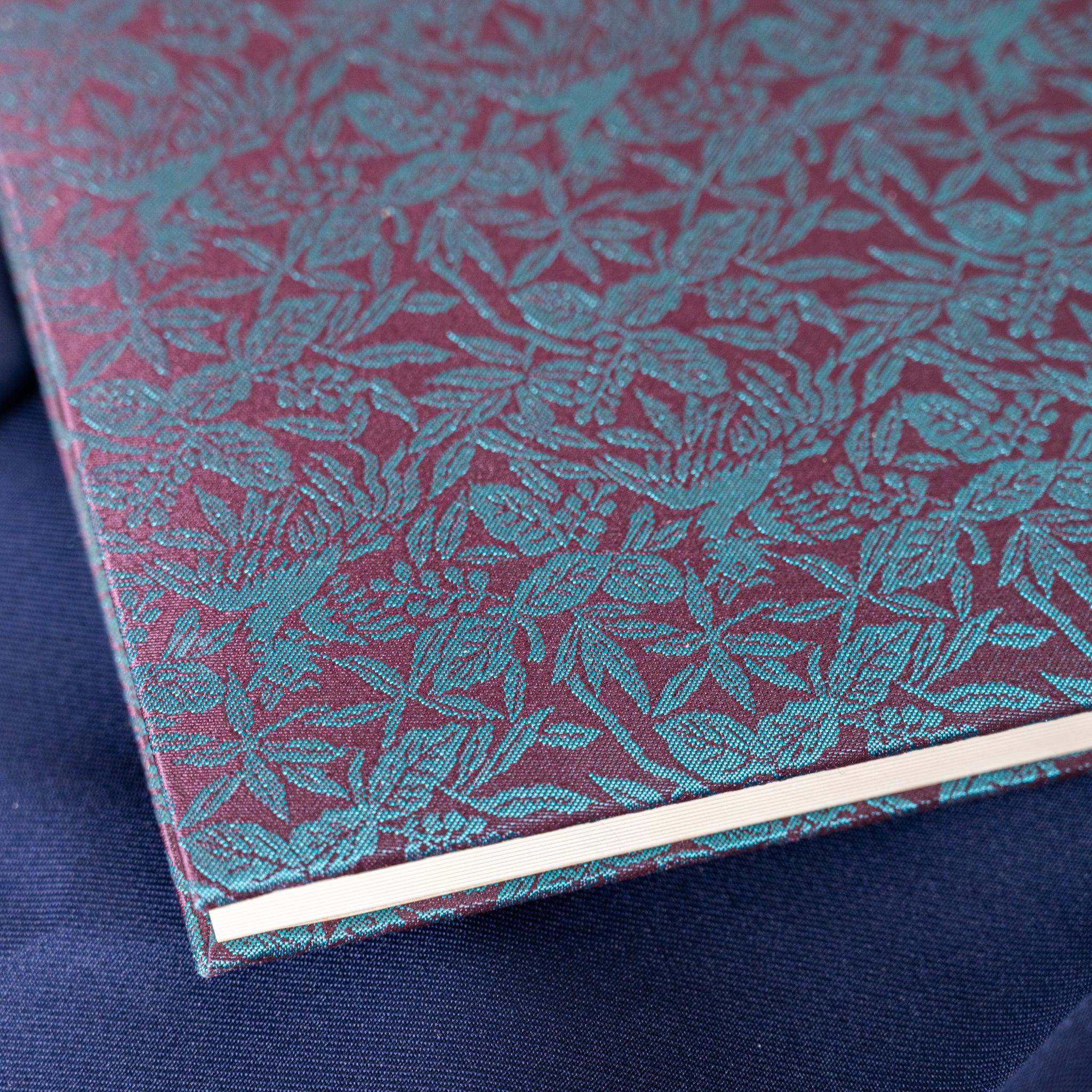 Kiri Take Ho-o Nishijin silk notebook top corner showing teal woven leaf pattern cover and white page edges below