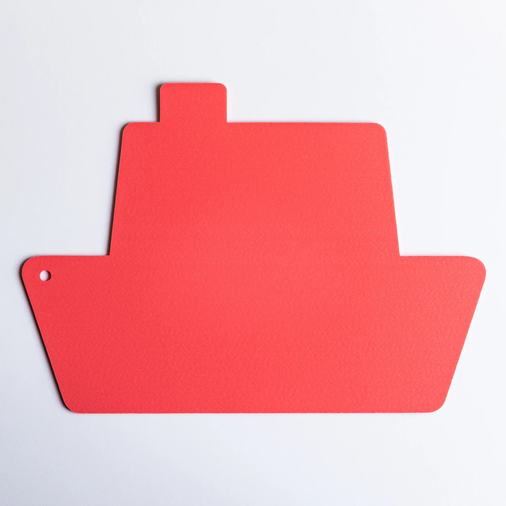 Red ship-shaped kitpas bath drawing board alone on a white surface, showing its simple silhouette and hole in the corner.