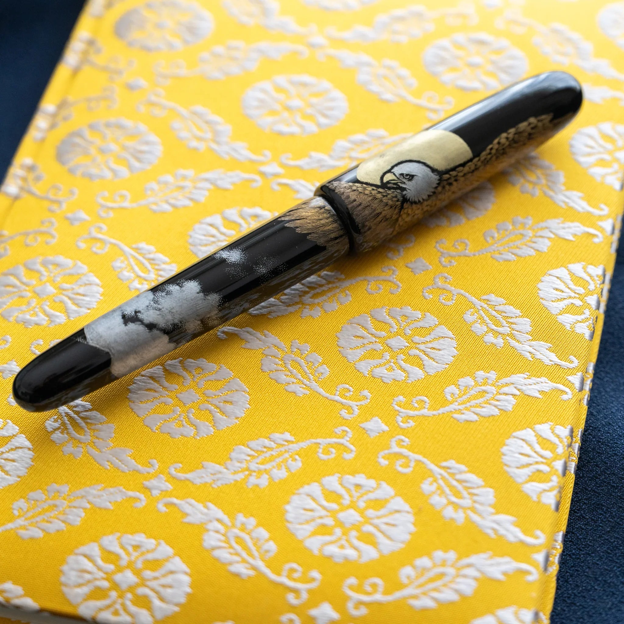 Ko Aoi Nishijin silk Homeicho notebook on dark fabric with decorative fountain pen placed diagonally across golden cover
