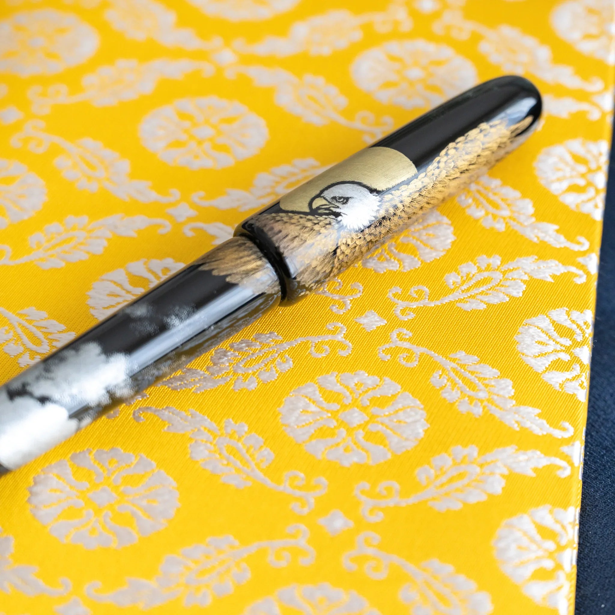 Close-up of maki-e fountain pen on Ko Aoi Nishijin silk cover showing golden floral weave and pen lacquer art detail