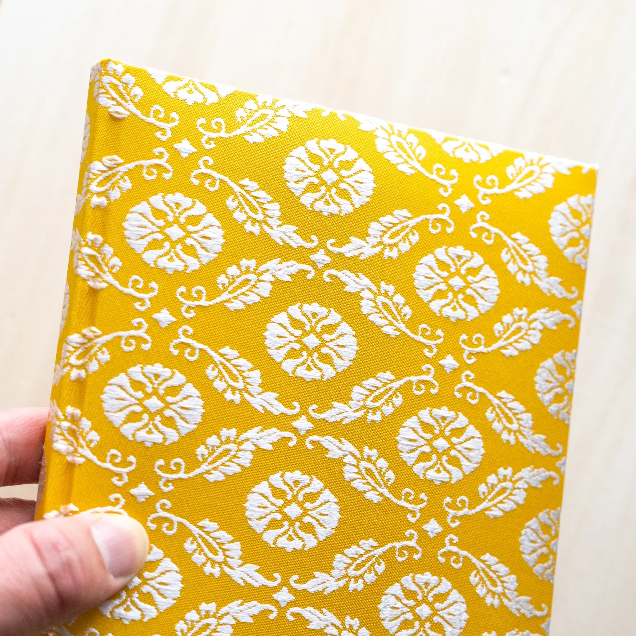 Hand holding Ko Aoi Nishijin silk Homeicho notebook showing full golden Ko Aoi floral cover, no paper band
