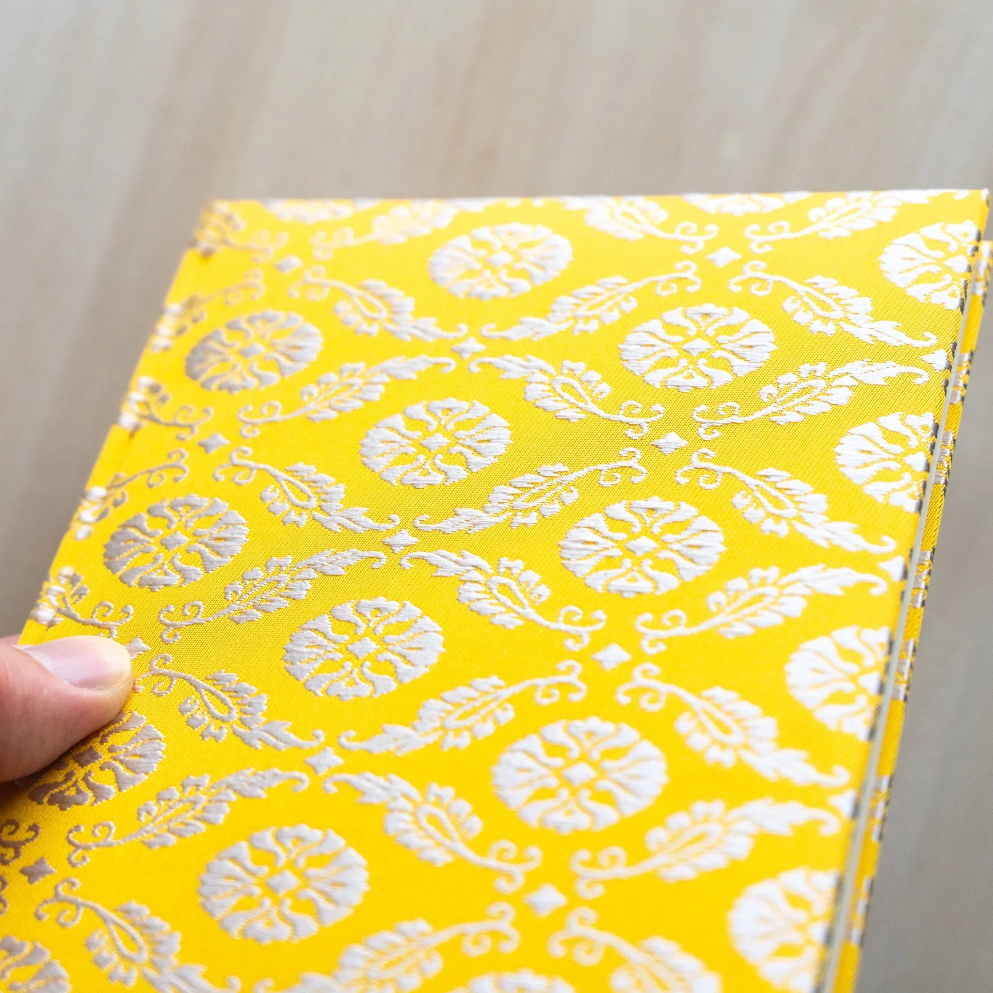 Angled corner close-up of Ko Aoi Nishijin silk cover showing golden Ko Aoi floral weave pattern and fabric binding edge