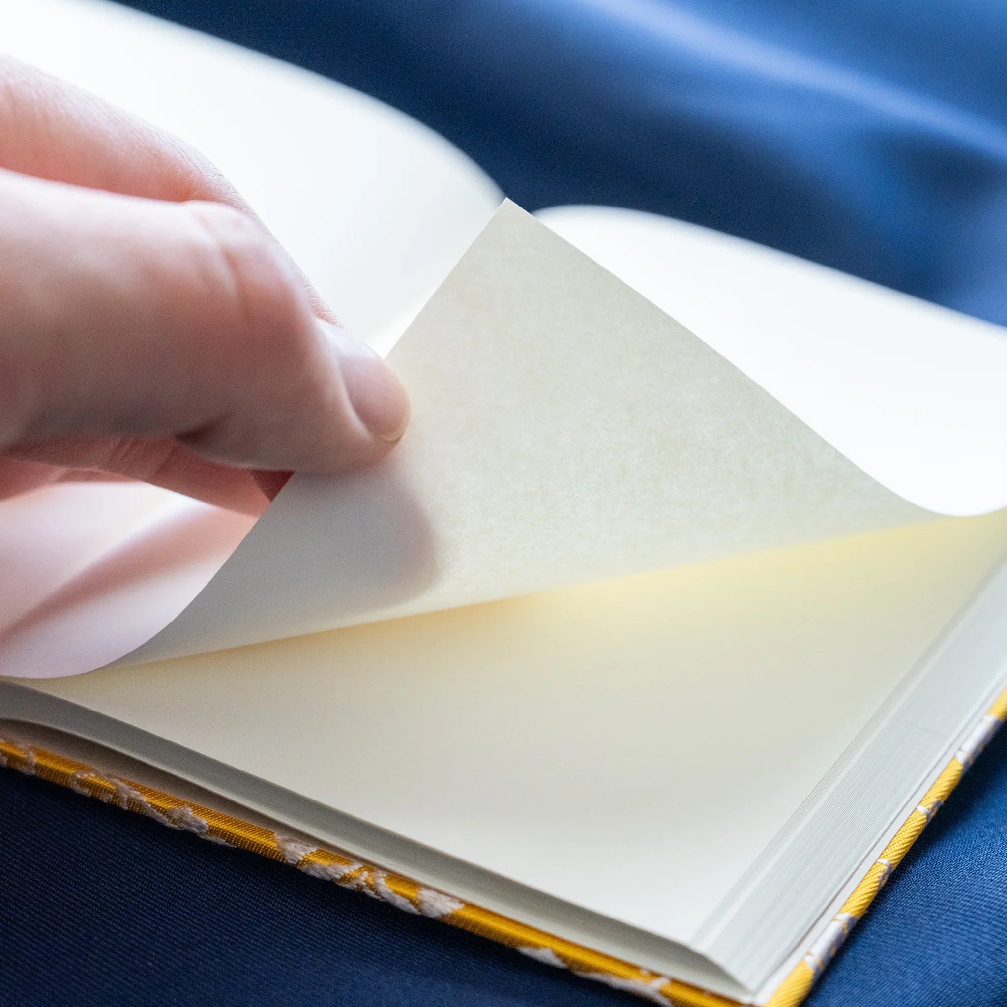 Hand flipping page of Ko Aoi Nishijin silk Homeicho notebook showing smooth cream paper texture and golden cover edge