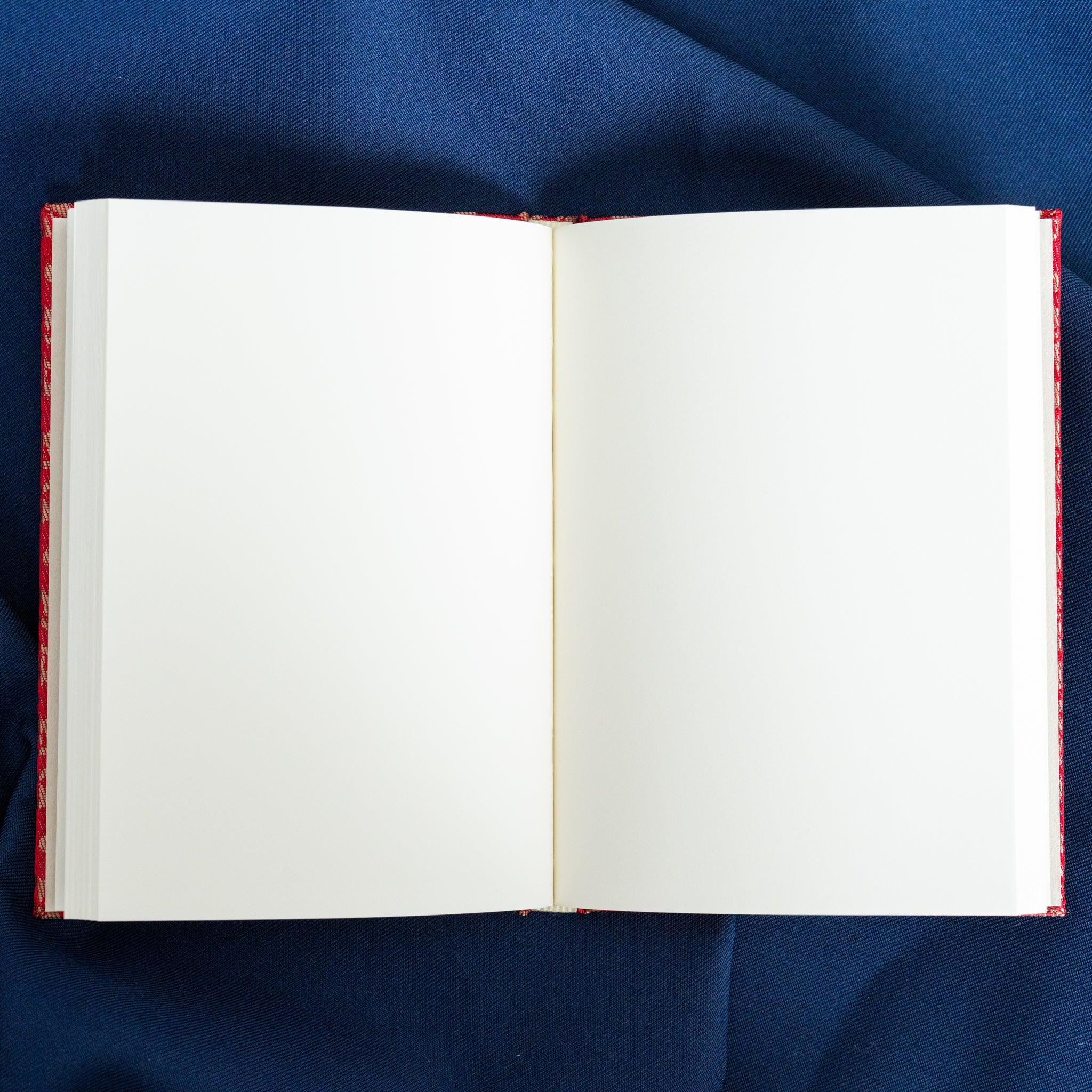 Ko Aoi Nishijin silk Homeicho notebook opened showing blank white page spread with vermilion cover border on blue fabric