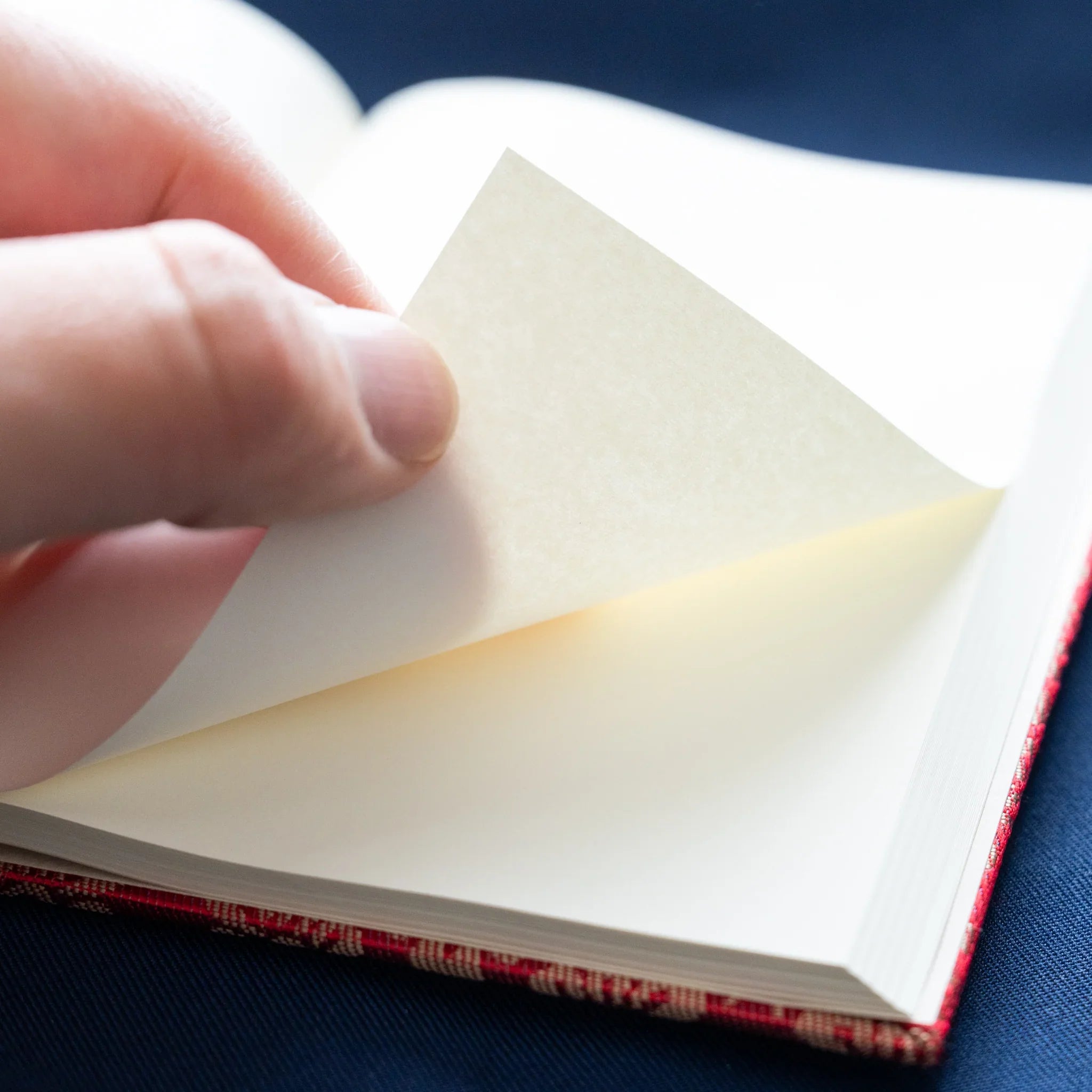 Hand flipping page of Ko Aoi Nishijin silk Homeicho notebook showing smooth cream paper and vermilion cover edge