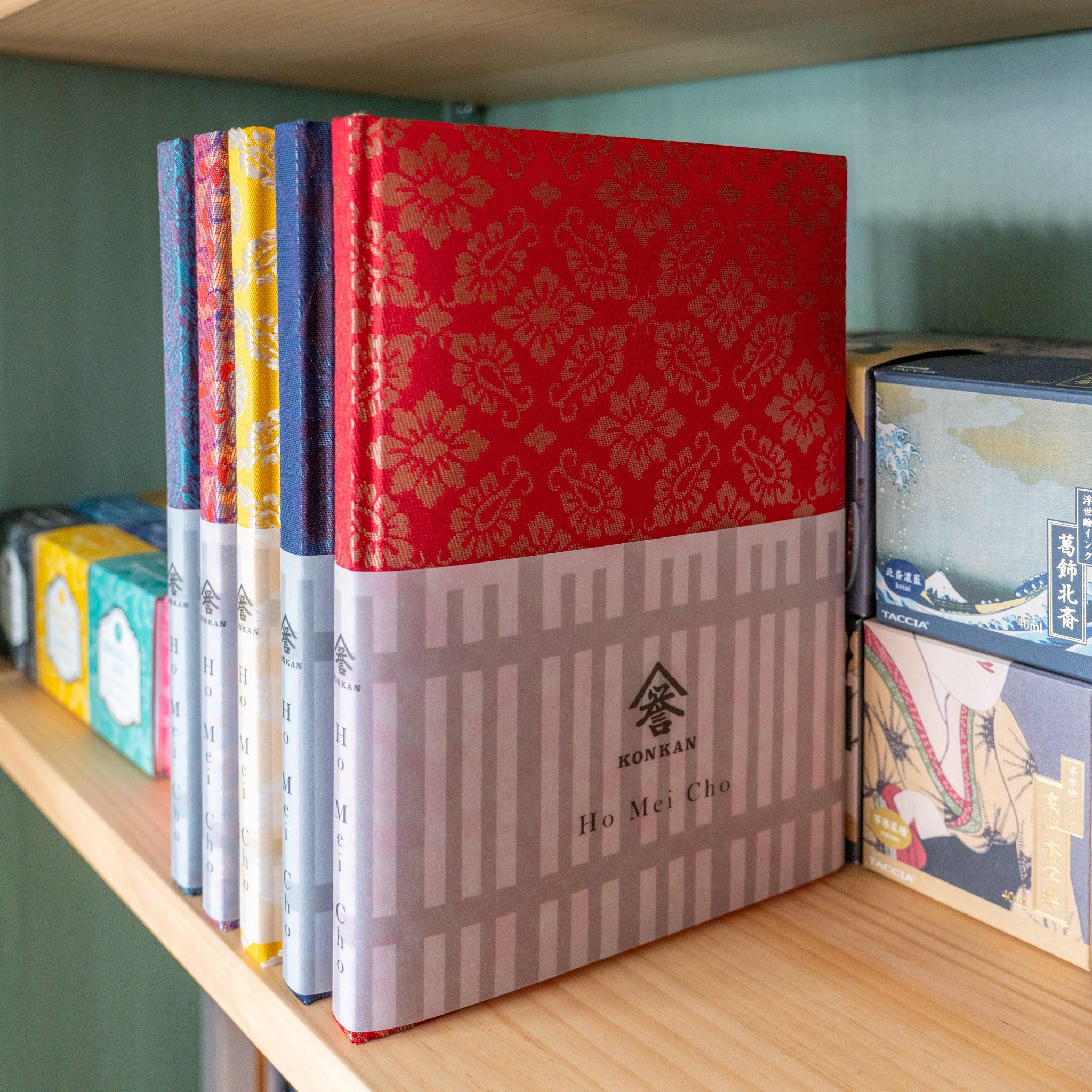 Ko Aoi Nishijin silk Homeicho notebook with KONKAN Ho Mei Cho band on shelf beside other Nishijin silk colorways