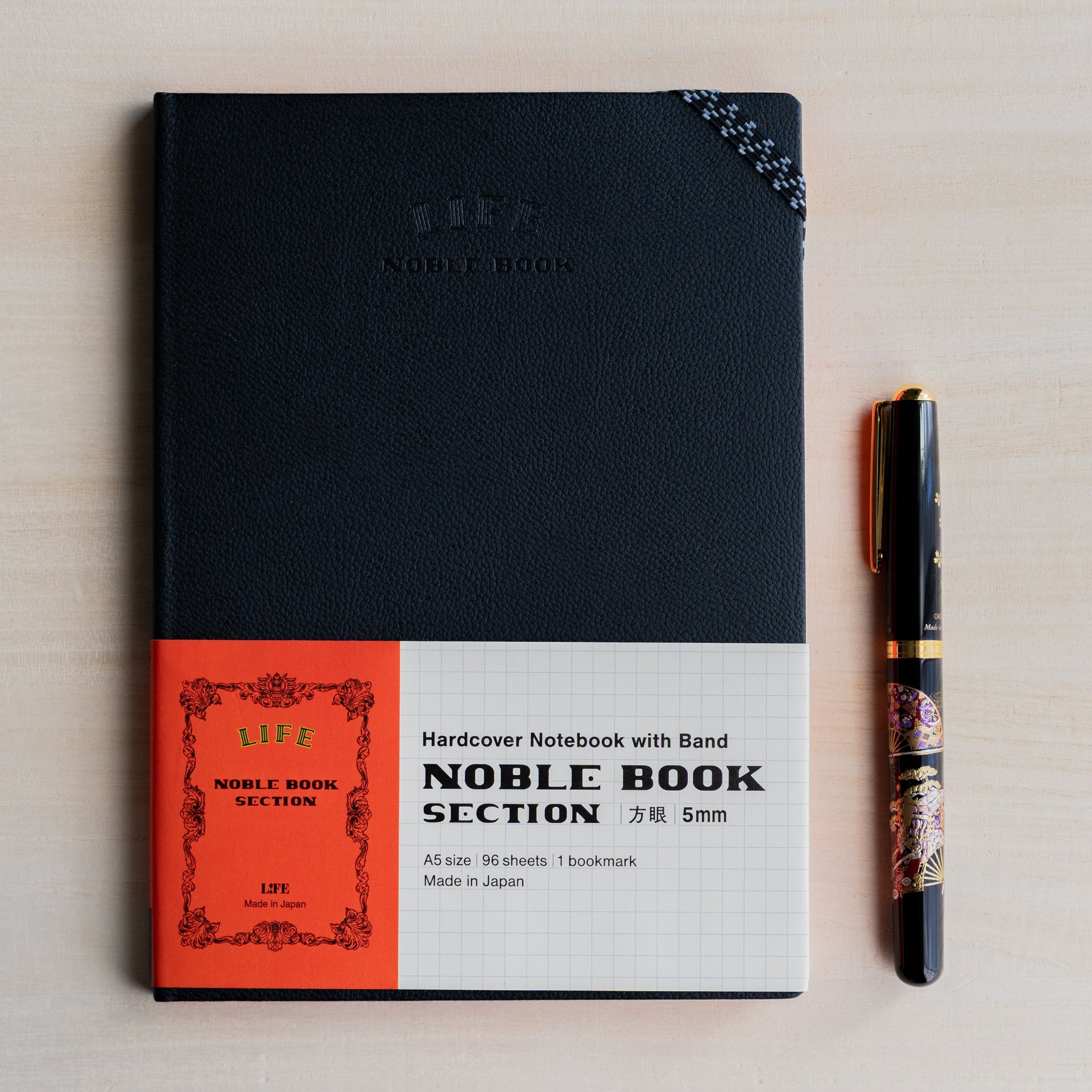Life noble hard cover notebook A5 shown flat with paper belly band, black textured cover and fountain pen placed beside