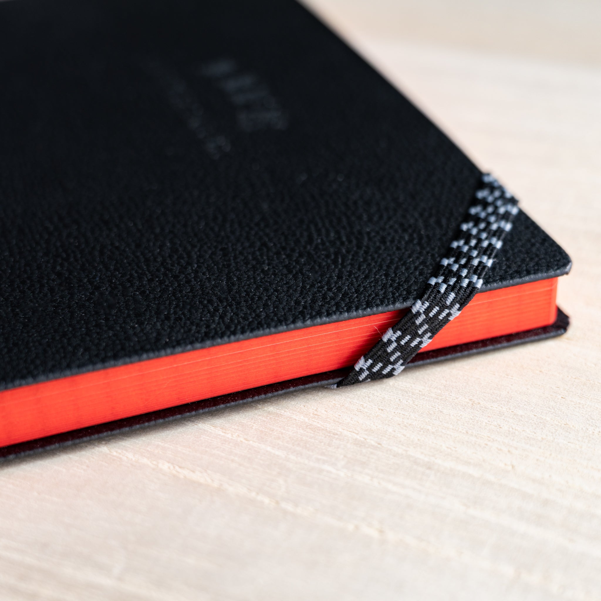 Life noble hard cover notebook A5 close-up of black textured cover corner, red page edges, and woven ribbon bookmark