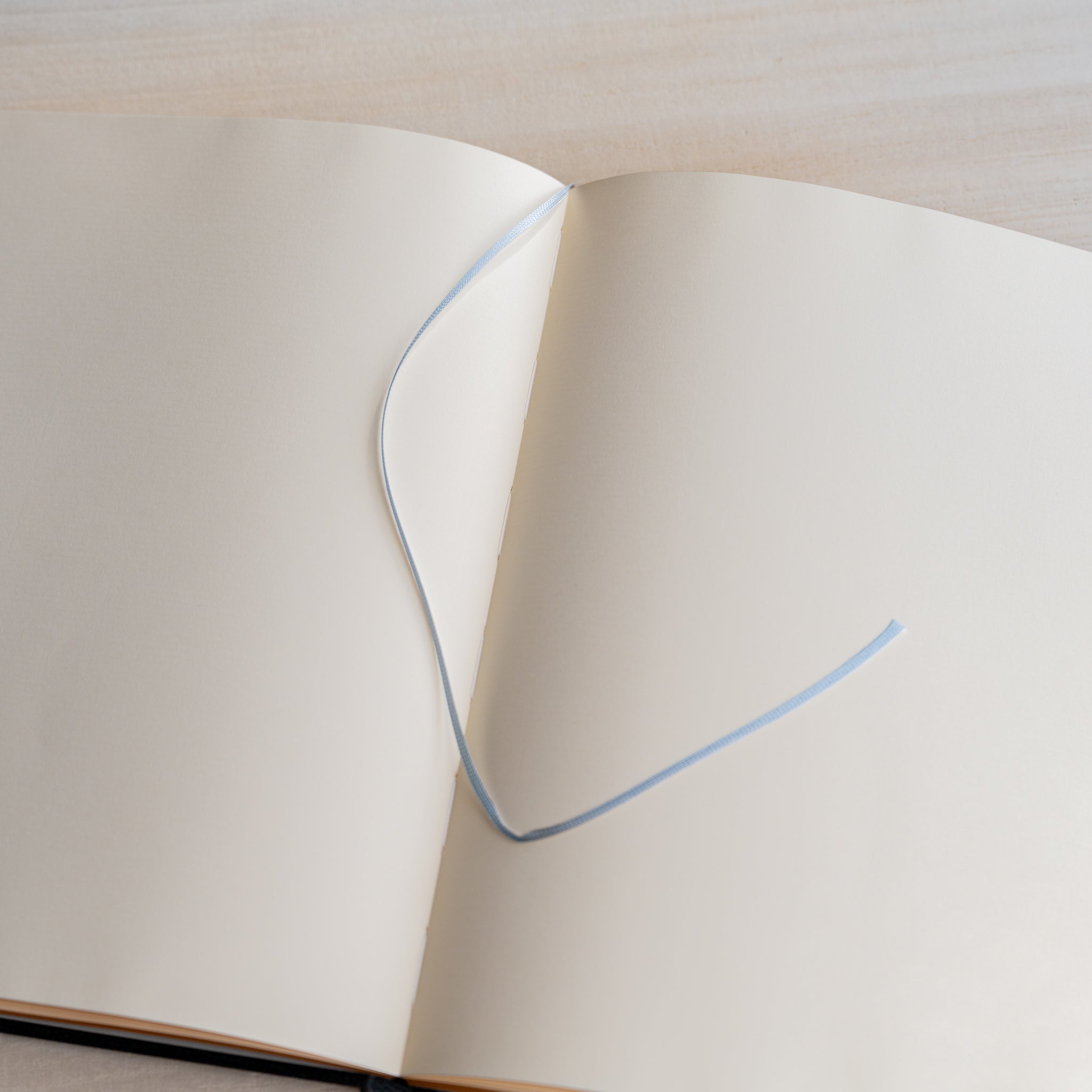 Life Noble notebook A5 open flat on desk, featuring cream fountain pen friendly pages and blue ribbon bookmark