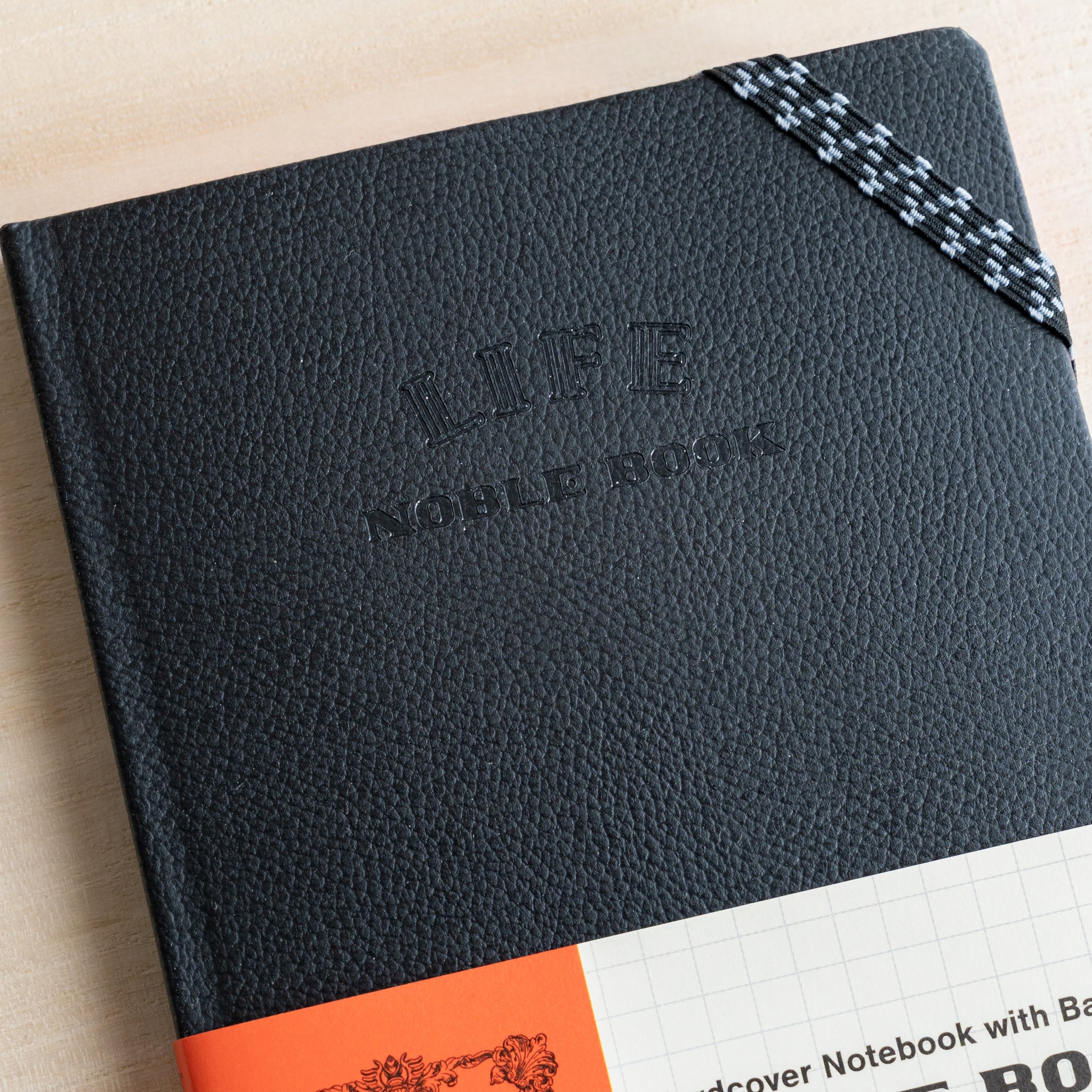 Life Noble notebook A6 hard cover close-up on desk, showing textured black cover, elastic band detail