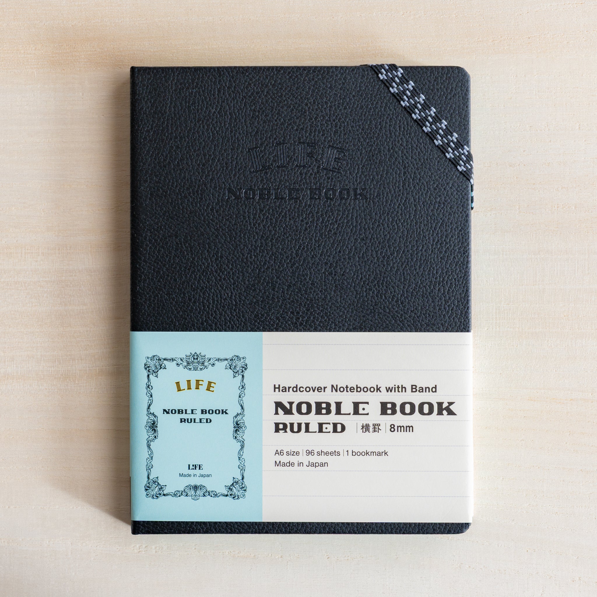 Life Noble notebook A6 front view with product band on desk, showing textured black hard cover