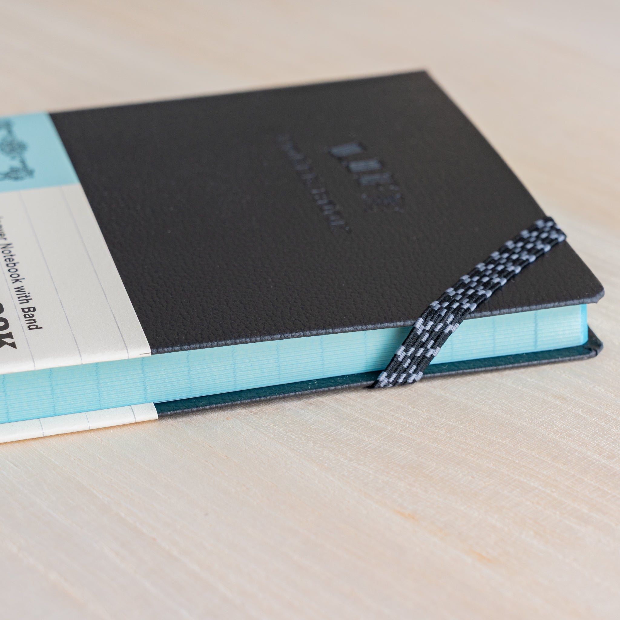 Life Noble notebook A6 hard cover side view on desk, showing elastic band, light blue page edges, and compact Japanese design