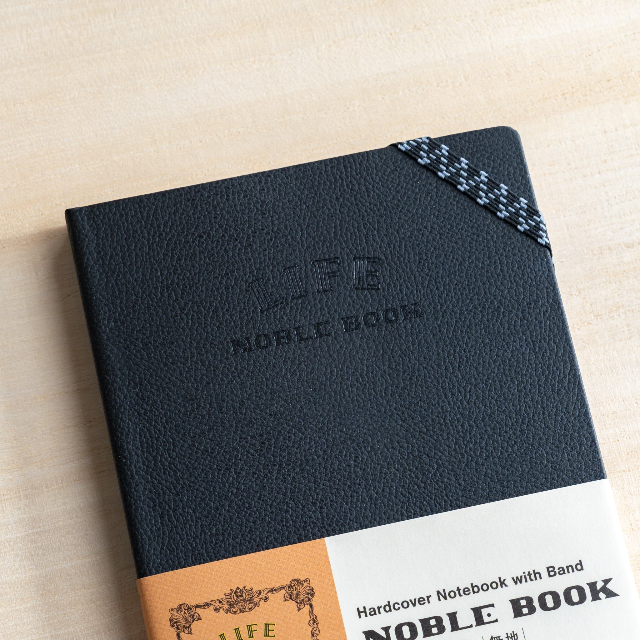 Life Noble notebook A6 hard cover with elastic band on desk, showing textured black cover and compact Japanese notebook design