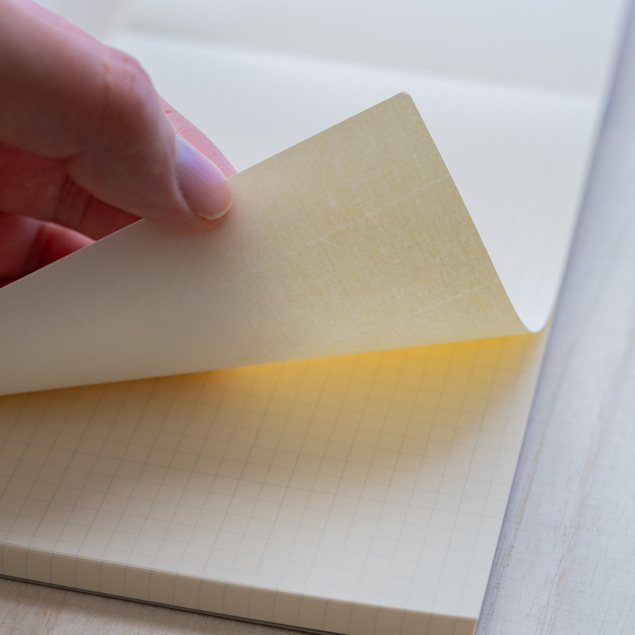 Life noble writing pad B6 close-up of grid L Writing Paper, sheet lifted by hand to show cream color, thickness, and texture