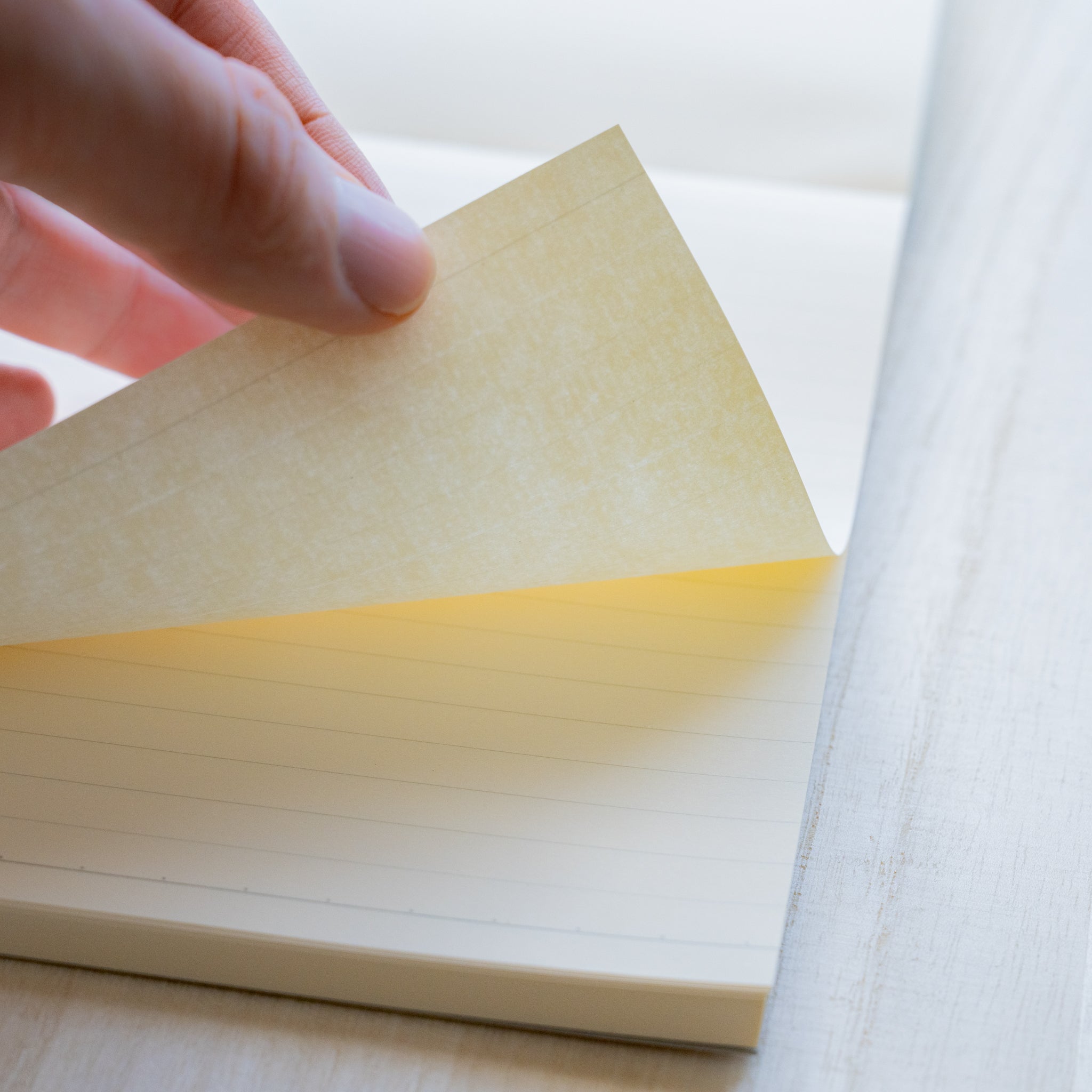 Life noble writing pad B6 close-up of blank L Writing Paper lifted by hand, ruled page visible beneath, showing paper color