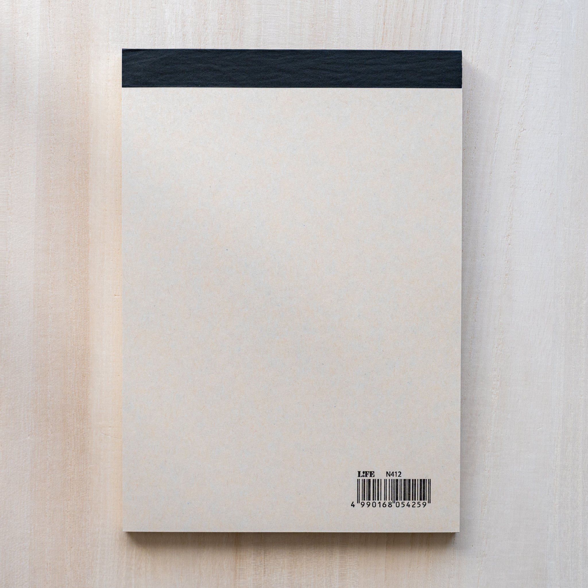 Life noble writing pad B6 back view shown flat, cream backing paper with black top binding and barcode on wood surface
