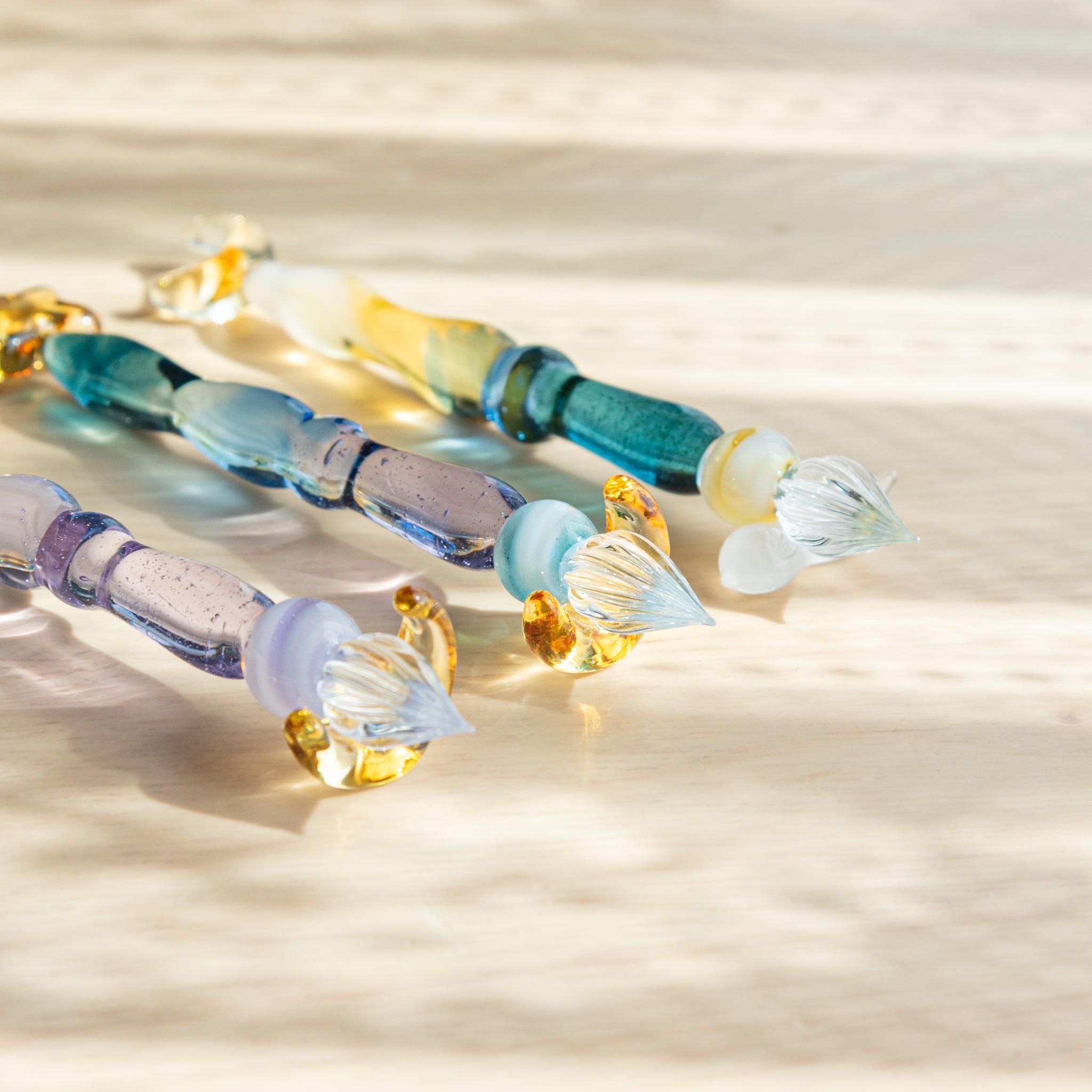 Close-up of the nibs of three glass pens with golden accents. The transparent glass and intricate details shimmer in the sunlight.