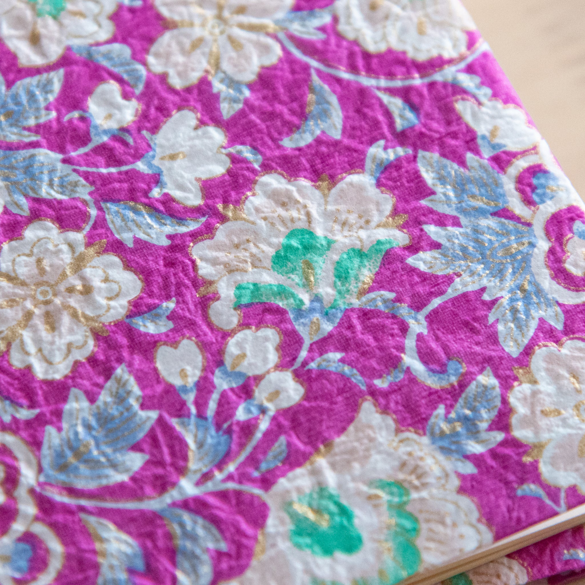 A close-up of a vibrant pink floral pattern featuring intricate white and green flowers, highlighting the detailed textures on the cover.