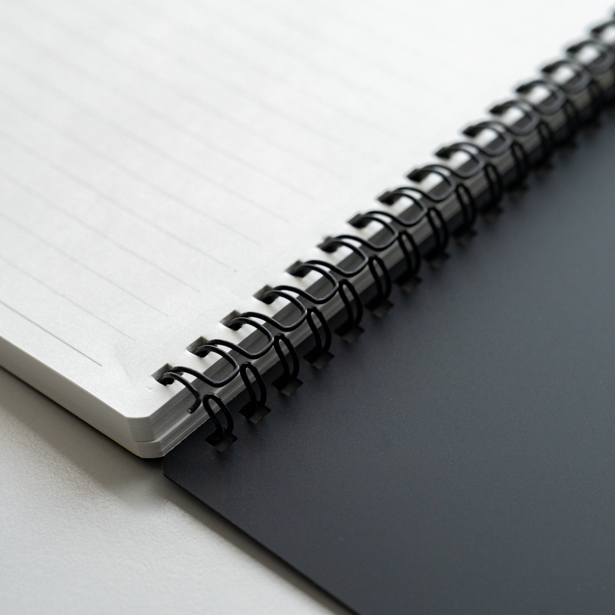 Close-up of Maruman Mnemosyne notebook with black spiral coil binding, lined pages and contrasting white paper and dark cover.