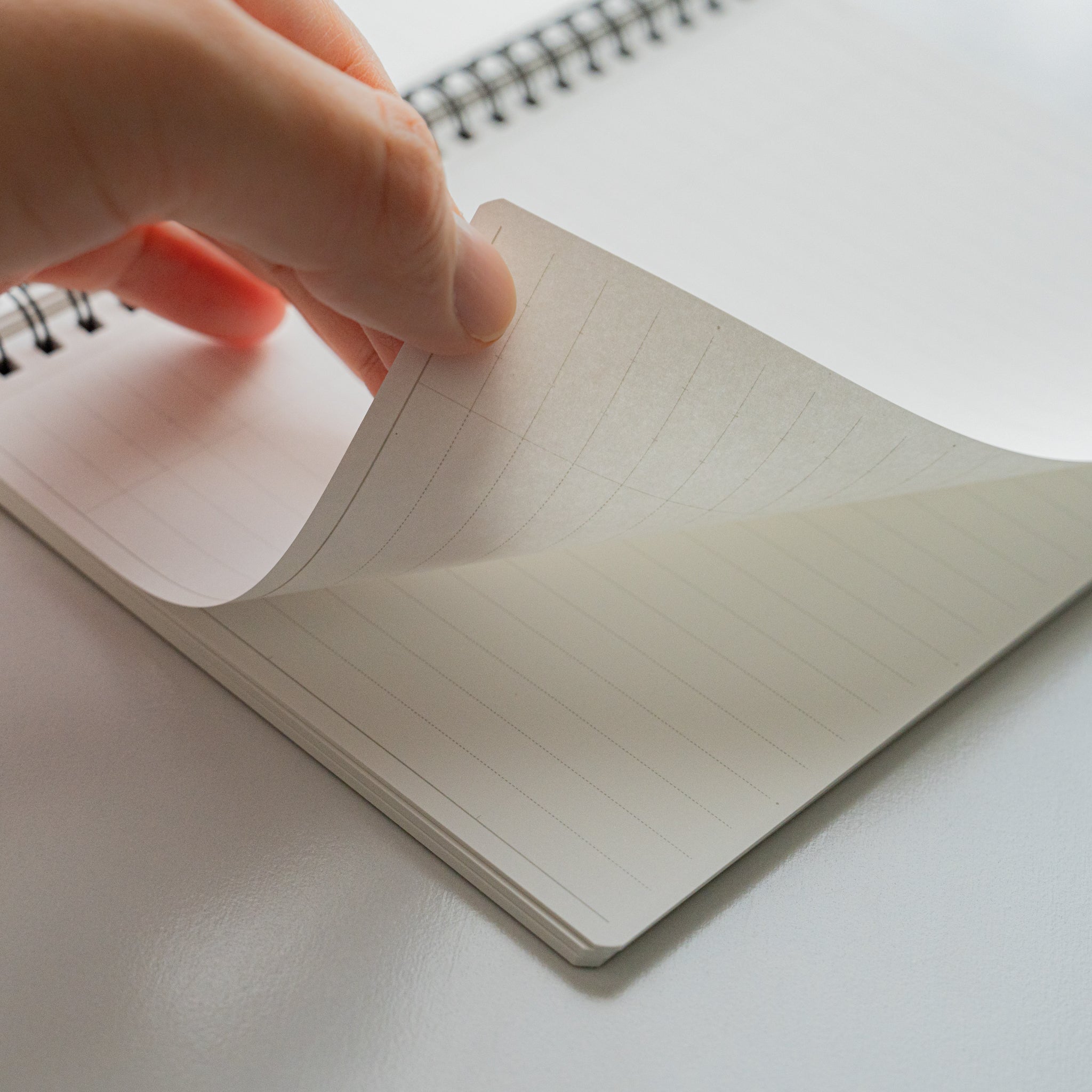 Hand flipping a page of Mnemosyne lined notebook, illustrating smooth writable paper and spiral binding for easy page turning