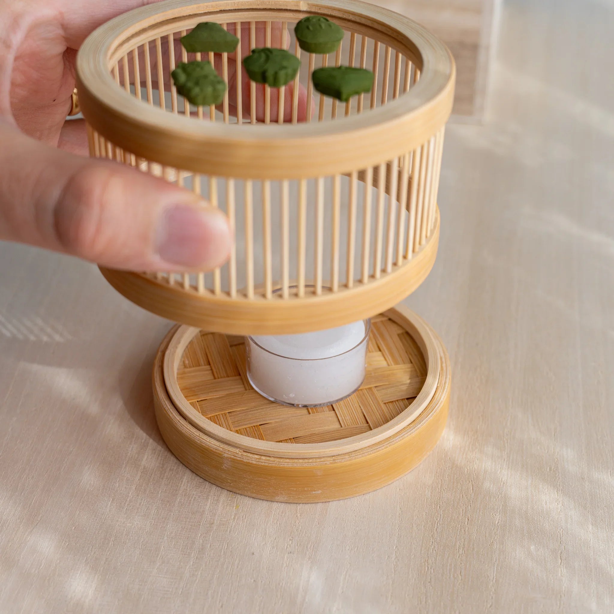 Hand placing tealight inside the woven bamboo base of the Suruga matcha incense tea warmer