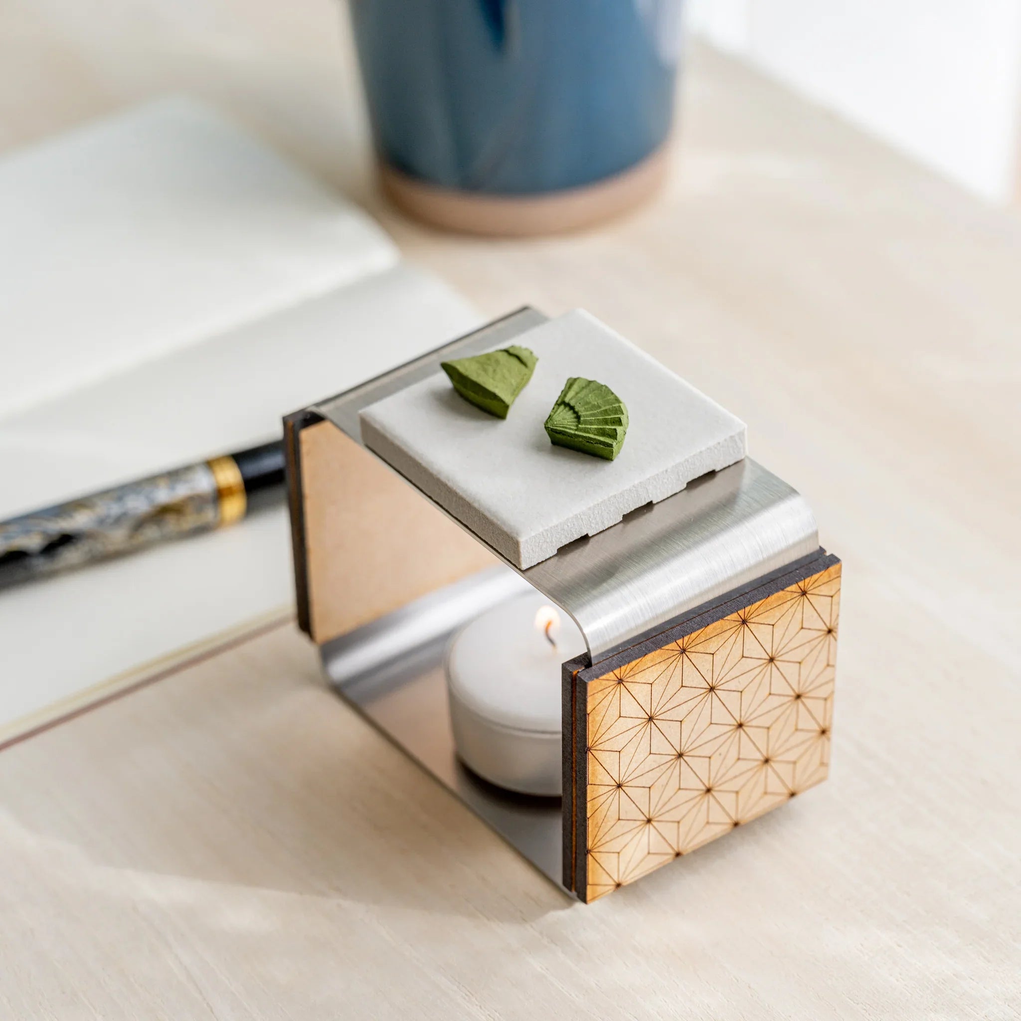 Foldable matcha incense tea warmer with asanoha wood walls, ceramic plate, two pressed matcha pieces, and lit tealight inside
