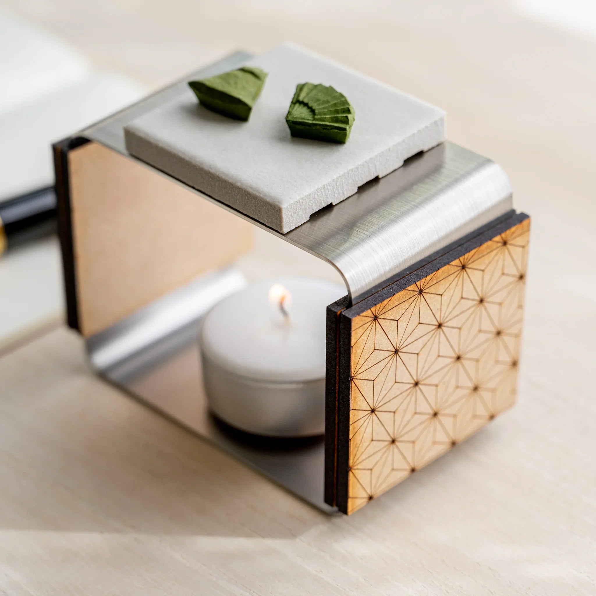 Close-up of matcha incense tea warmer showing asanoha laser-cut wood panel, ceramic plate, and lit tealight inside