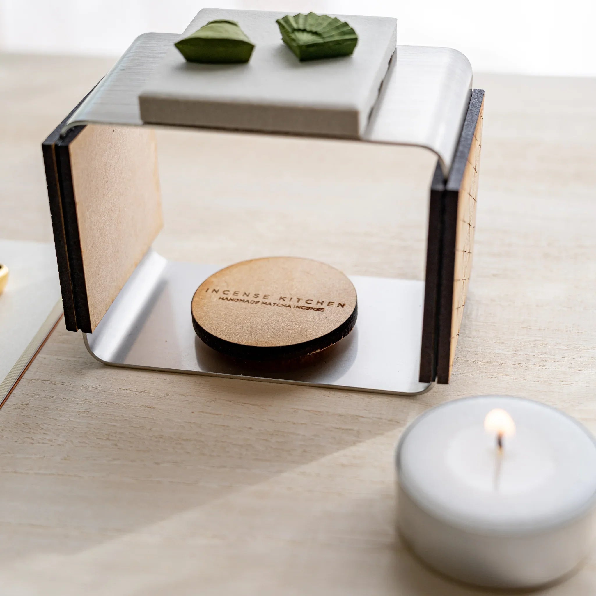 Foldable matcha incense tea warmer with INCENSE KITCHEN engraved cork pad inside and pressed matcha pieces on ceramic plate