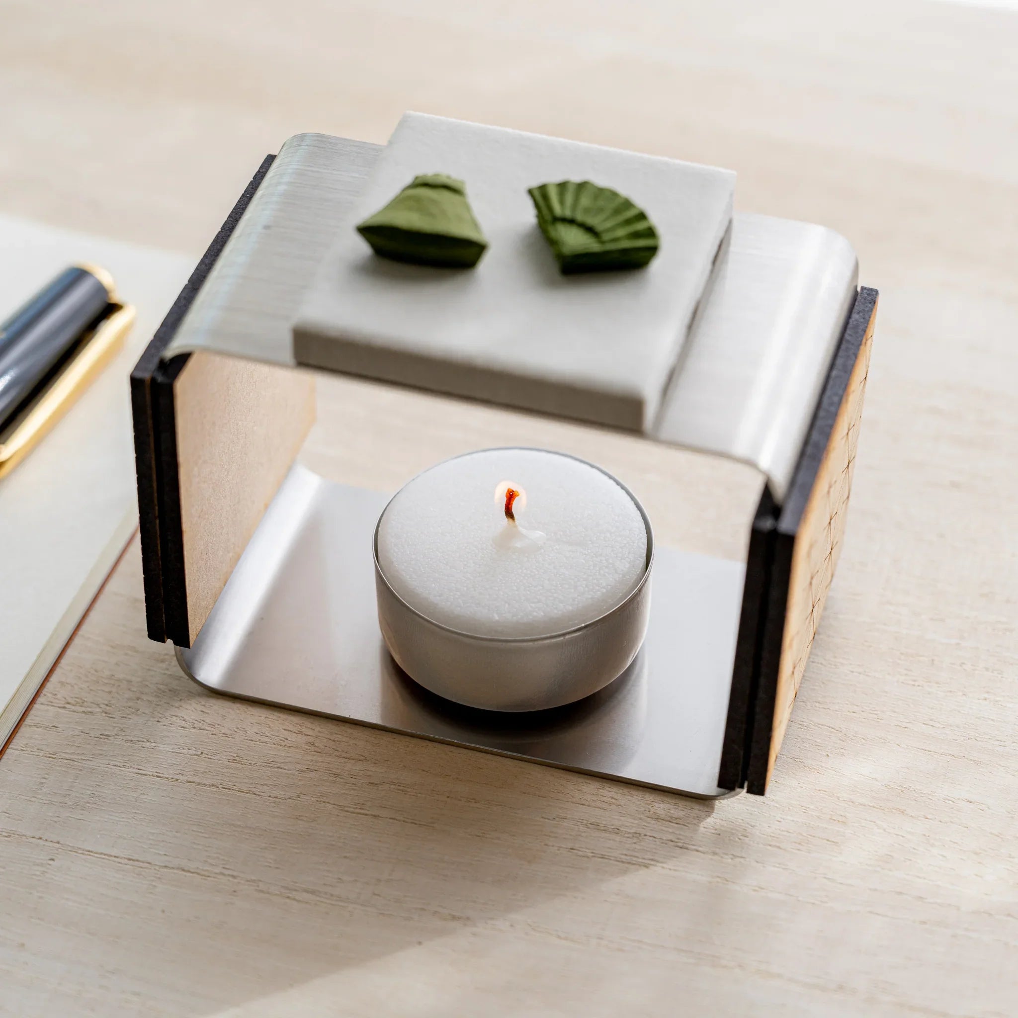 Lit tealight inside foldable matcha incense tea warmer with two pressed matcha pieces on the unglazed ceramic plate