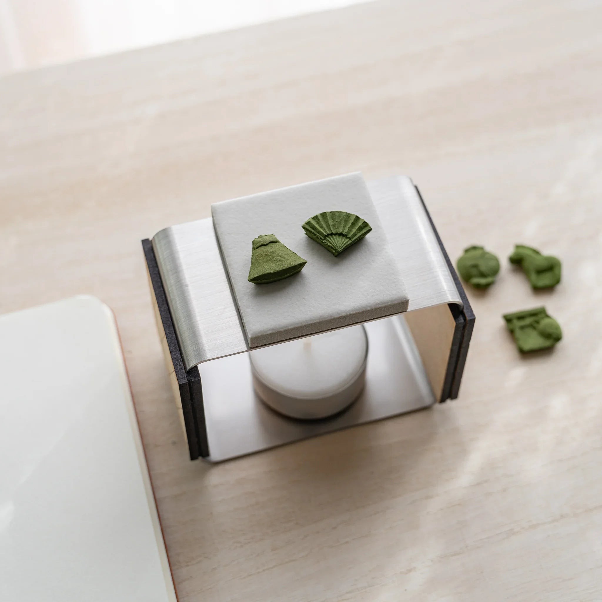 Foldable matcha incense tea warmer from above with five pressed matcha incense pieces in lucky-charm shapes nearby