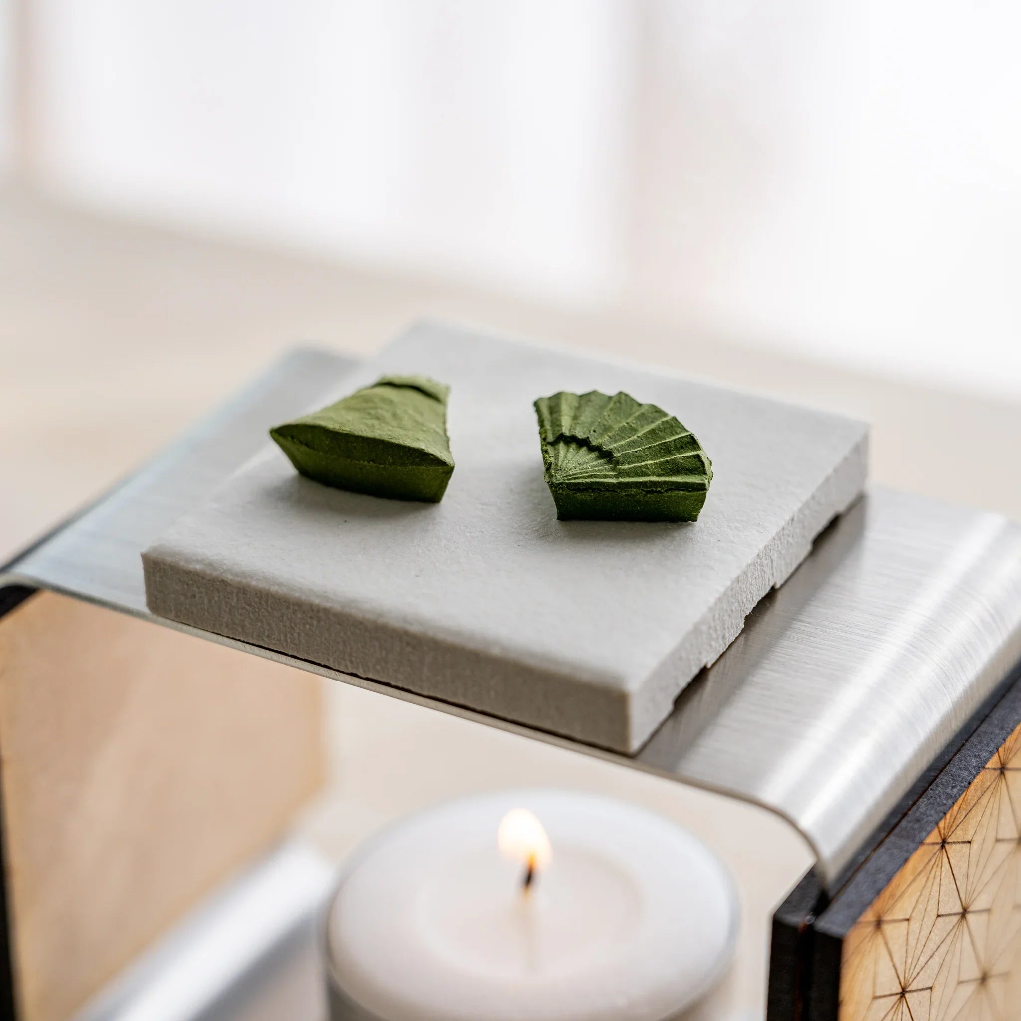 Two pressed matcha incense pieces on unglazed ceramic plate of the matcha incense tea warmer with lit tealight below