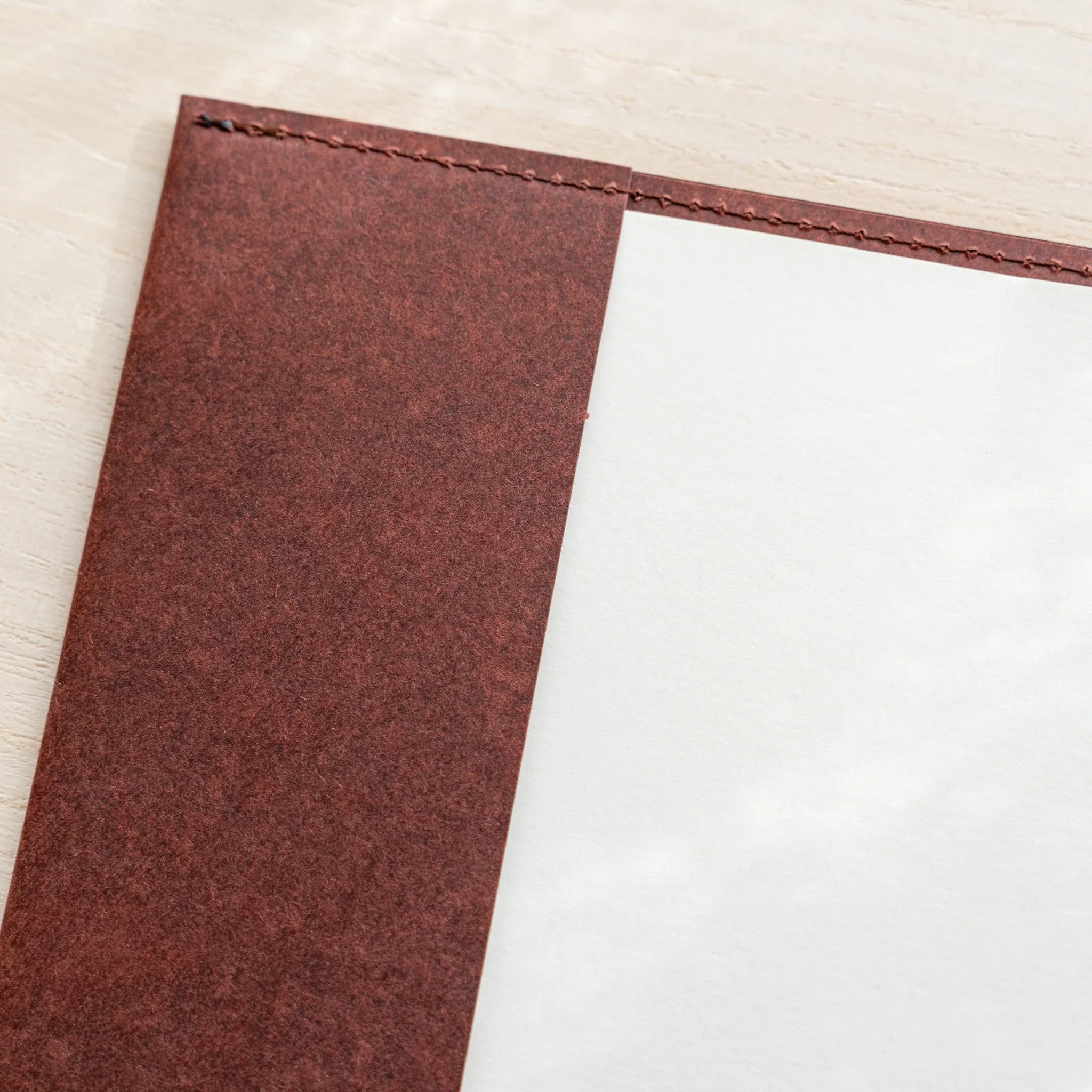 Close-up of Midori MD Notebook Hard Cover top-left corner, dark red hard paper with black stitched edges, white inner panel