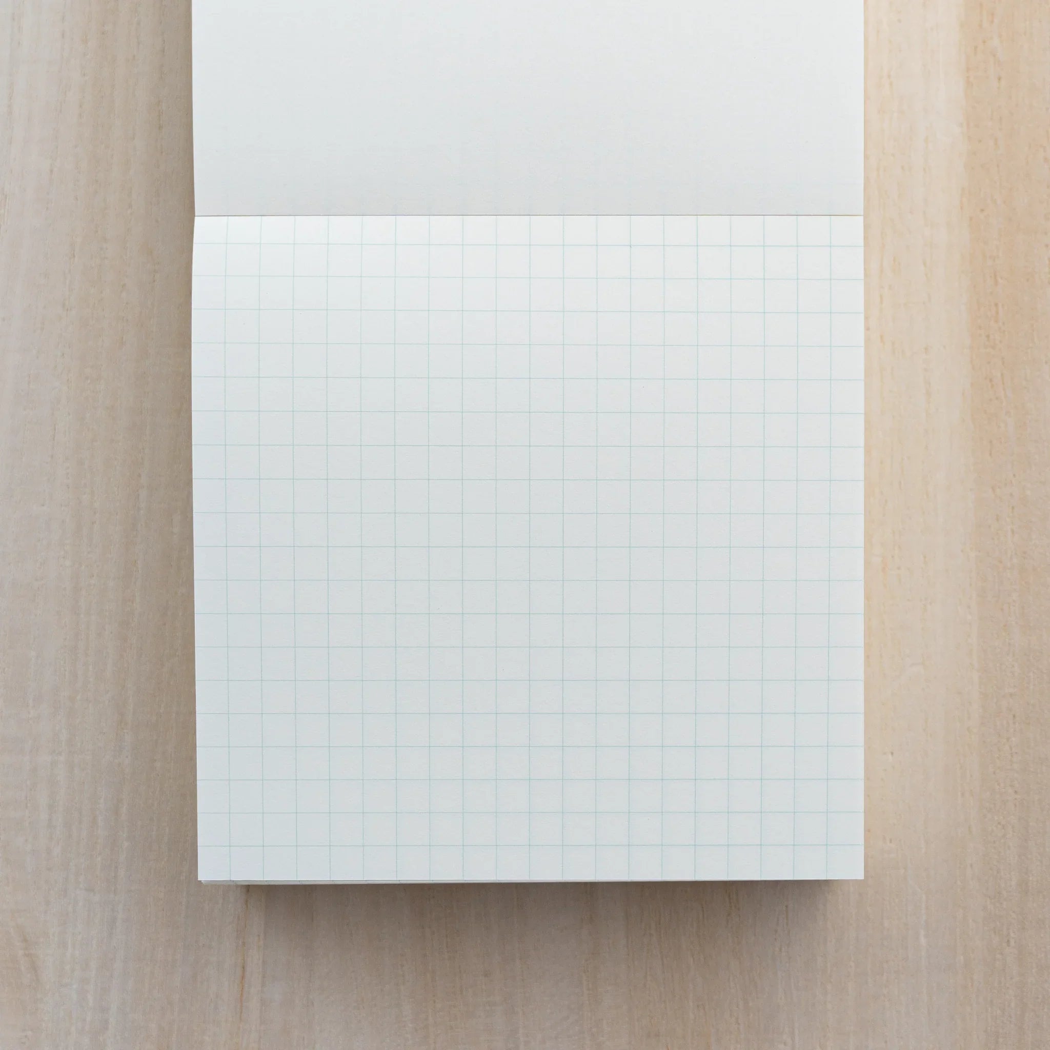 MD Memo Block opened to a sheet with a light blue grid, top sheet folded back, on wood