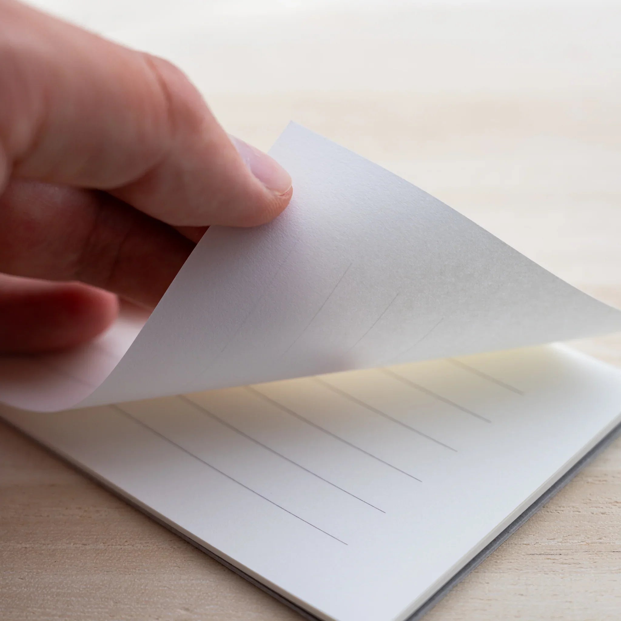 Hand lifting a sheet of MD Paper Cotton letter pad showing cream paper with vertical ruled lines
