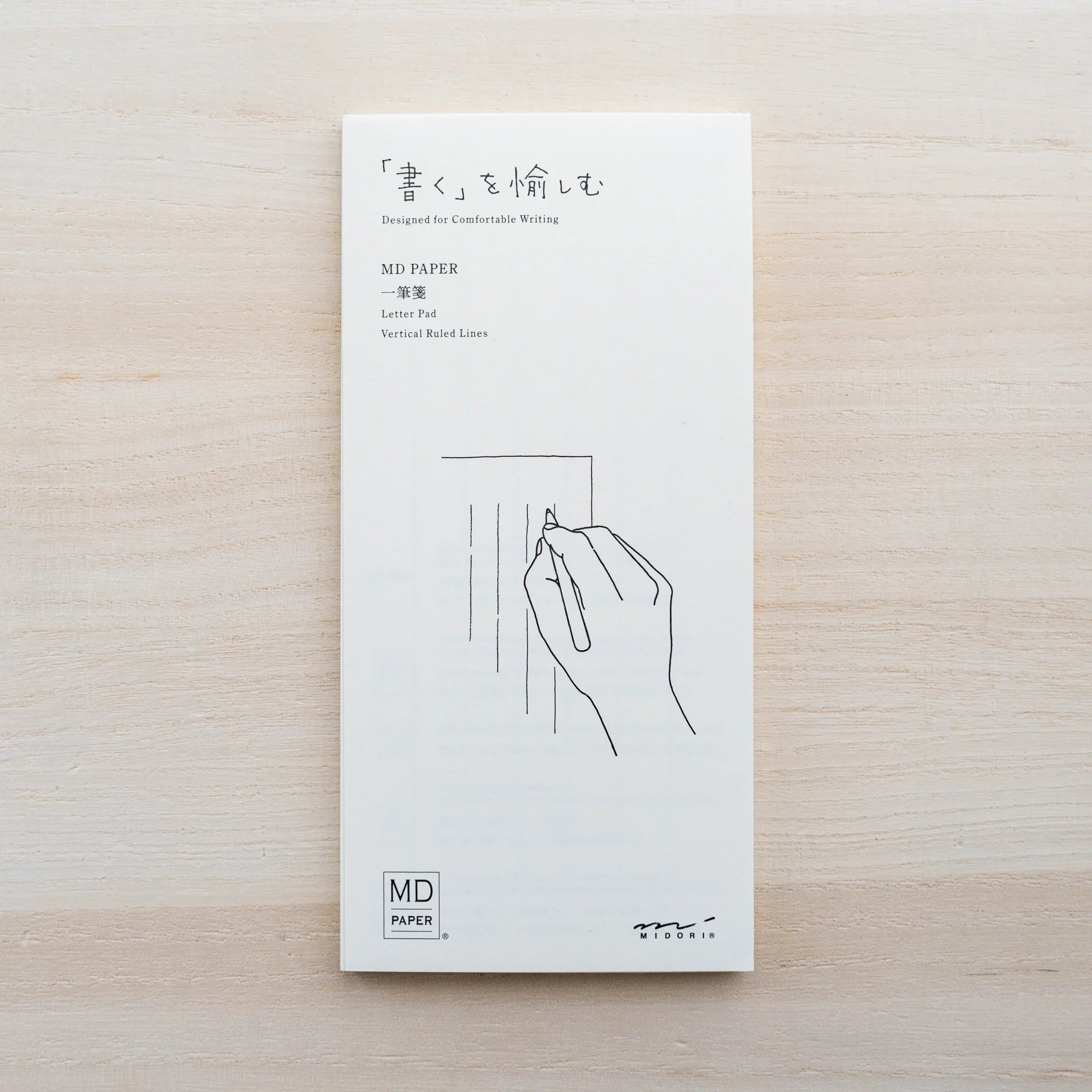 Front of an MD Paper letter pad cover with black hand-and-pen illustration and MD Paper and Midori logos on wood